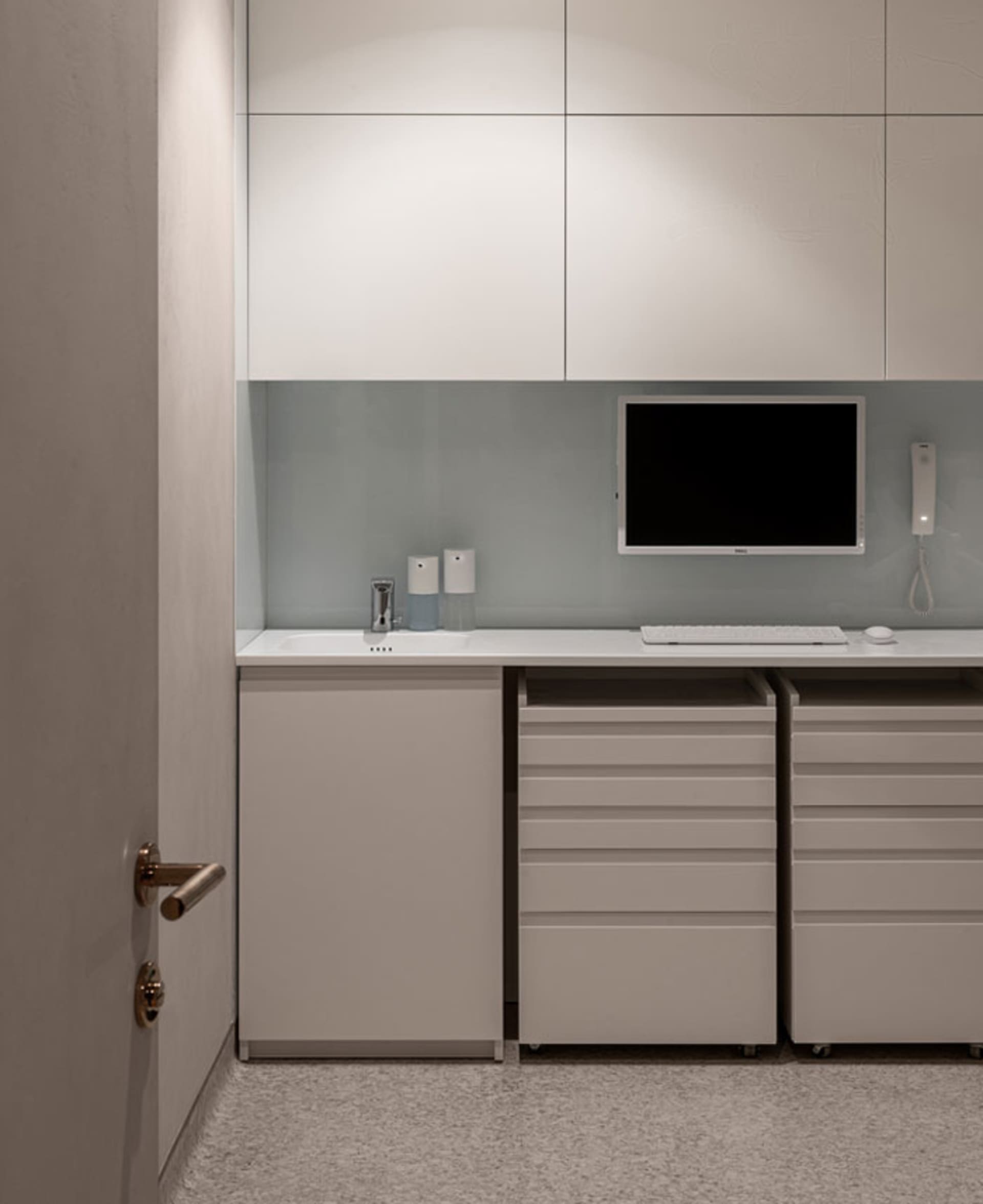 A minimalist office space with a white desk, drawers, and cabinets.