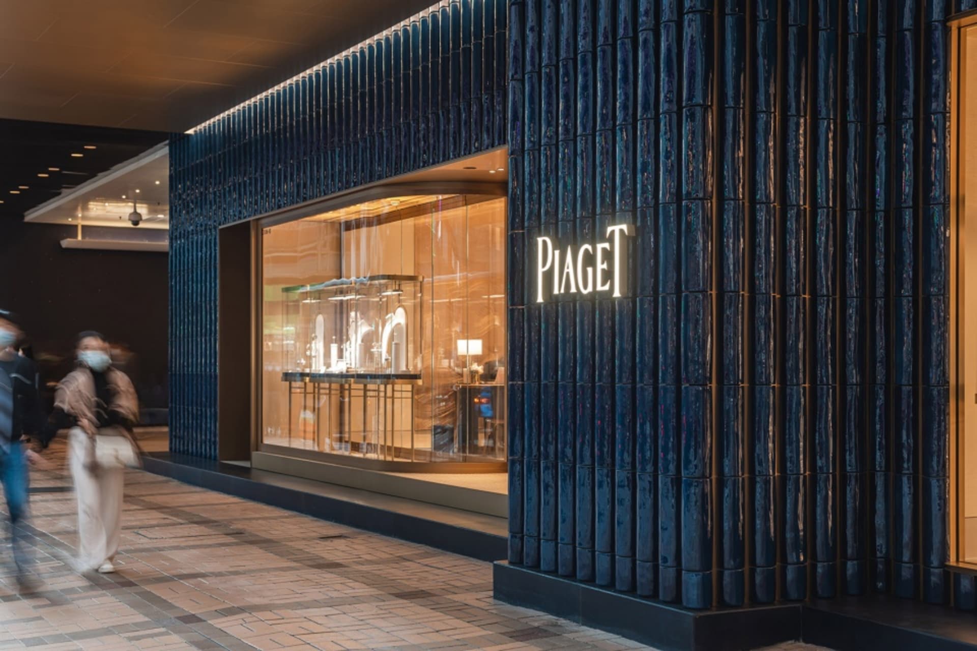 A storefront with metallic tiles and illuminated signage for Piaget.