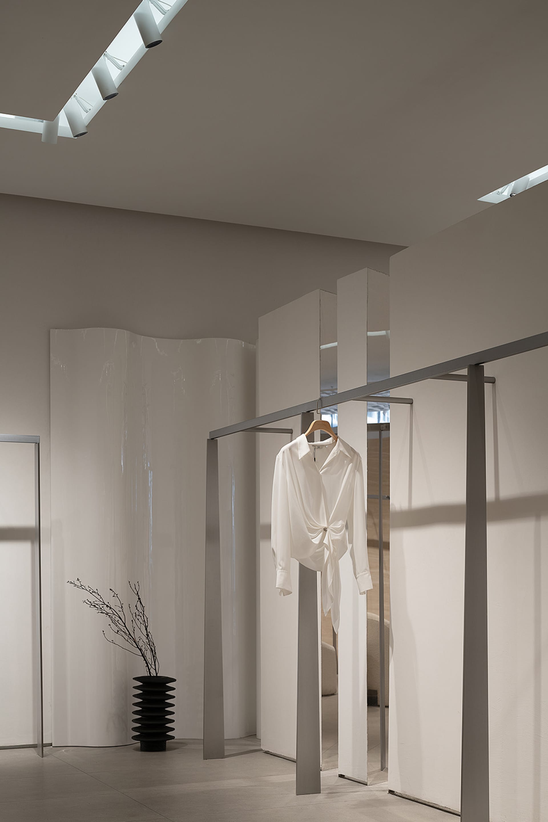 現代簡約服飾店室內,白色牆面、玻璃面板,以及單件白色襯衫懸掛在衣架上。