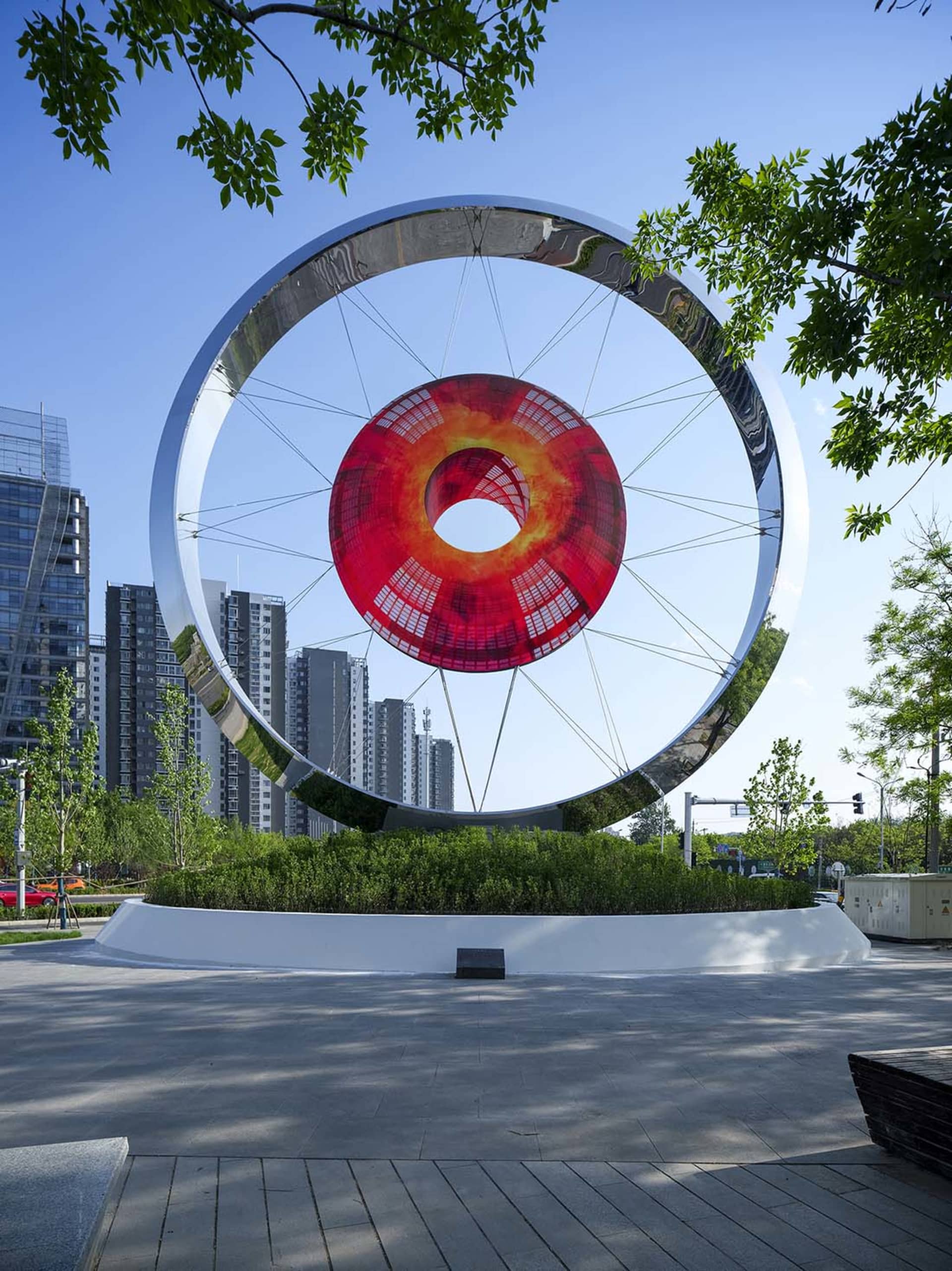 A modern urban sculpture featuring a red circular screen and a metallic circular frame.