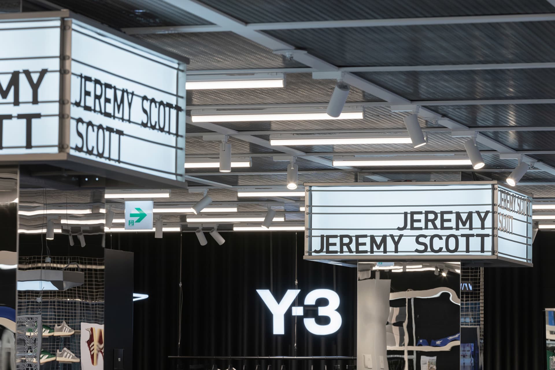 一處零售空間,展示以 Jeremy Scott 與 Y-3 為名的發光招牌,呈現現代照明設計。