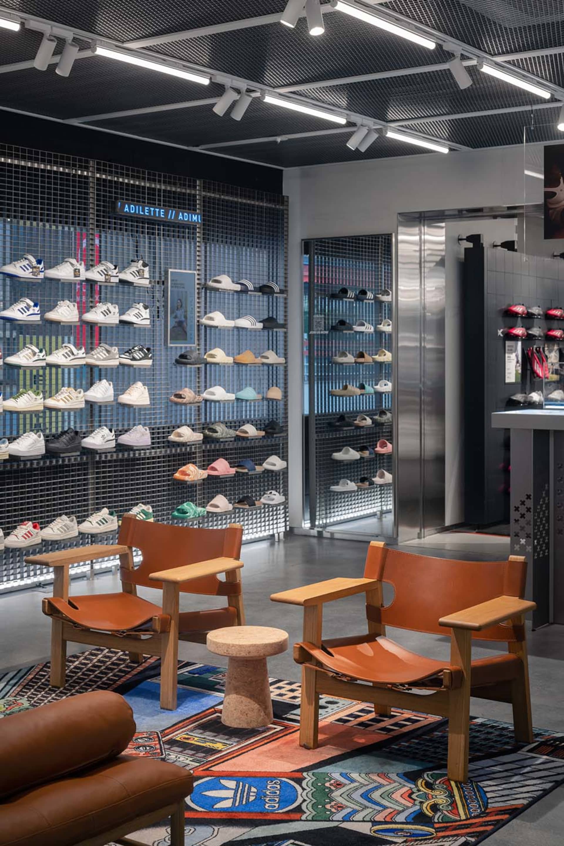 A retail interior featuring a metal grid display wall showcasing various styles of shoes in a store.