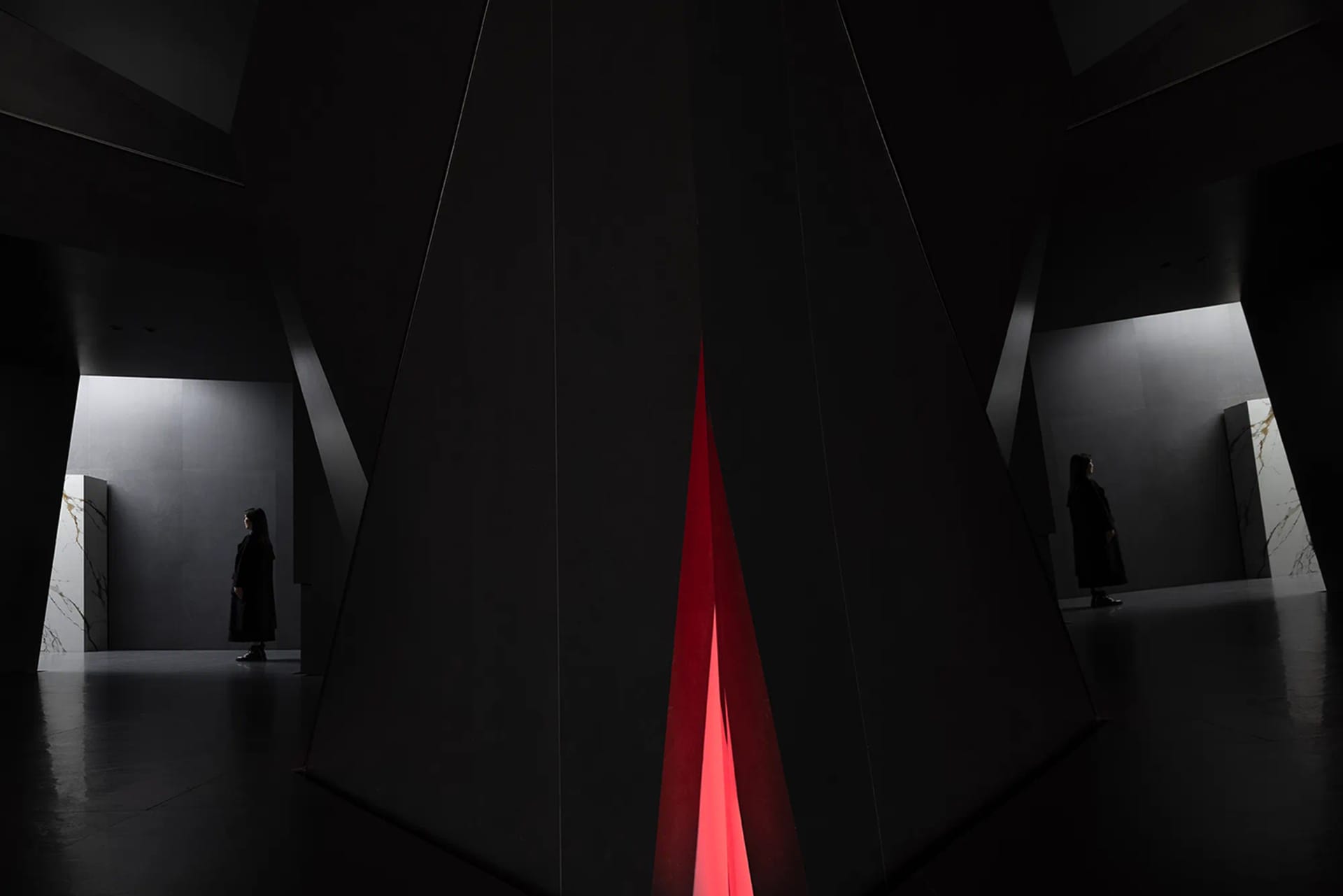Two individuals standing in a modern black interior space with a glass wall and red light