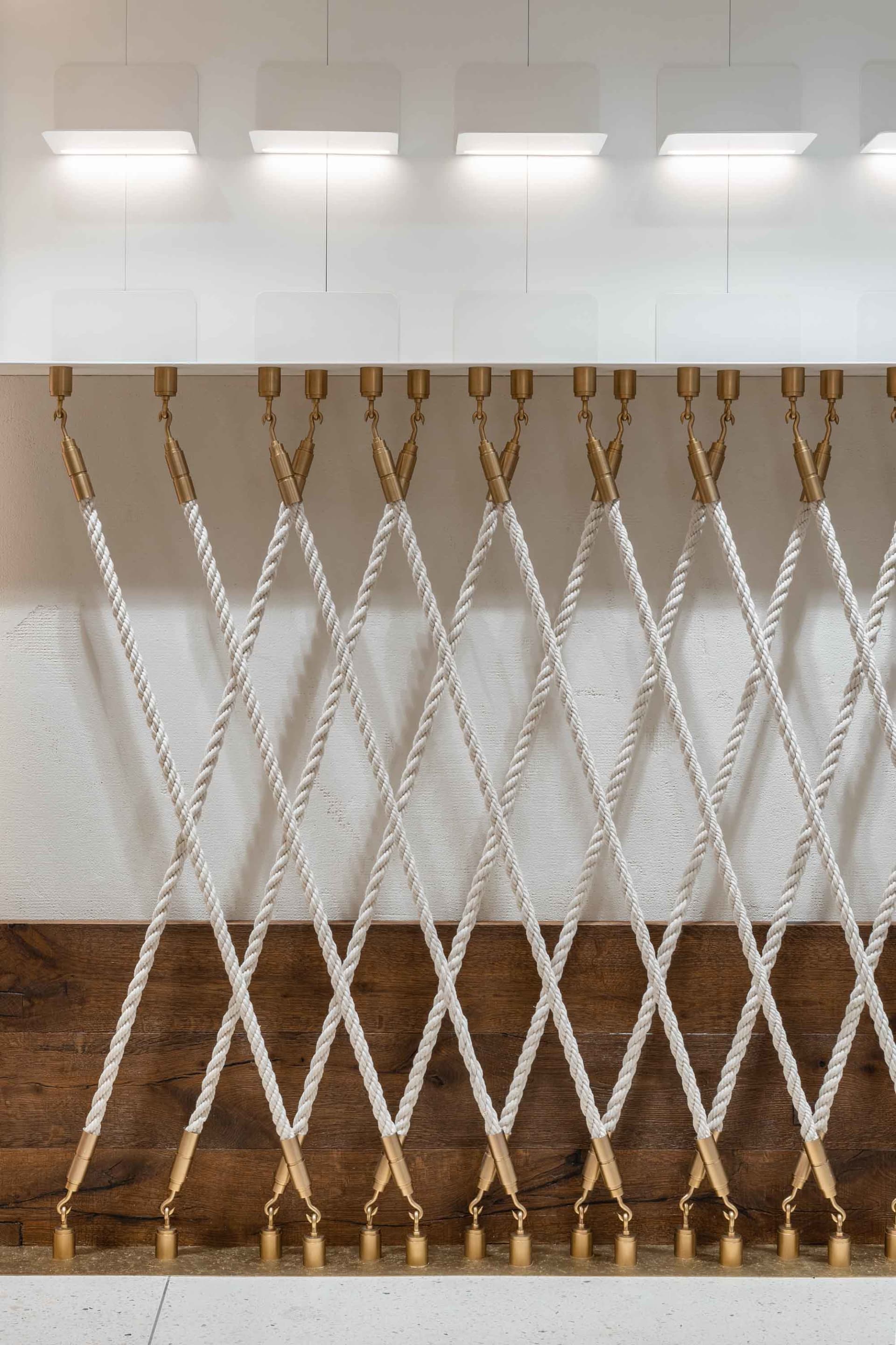 Textile cords suspended from brass hooks in a modern lighting exhibition setting.