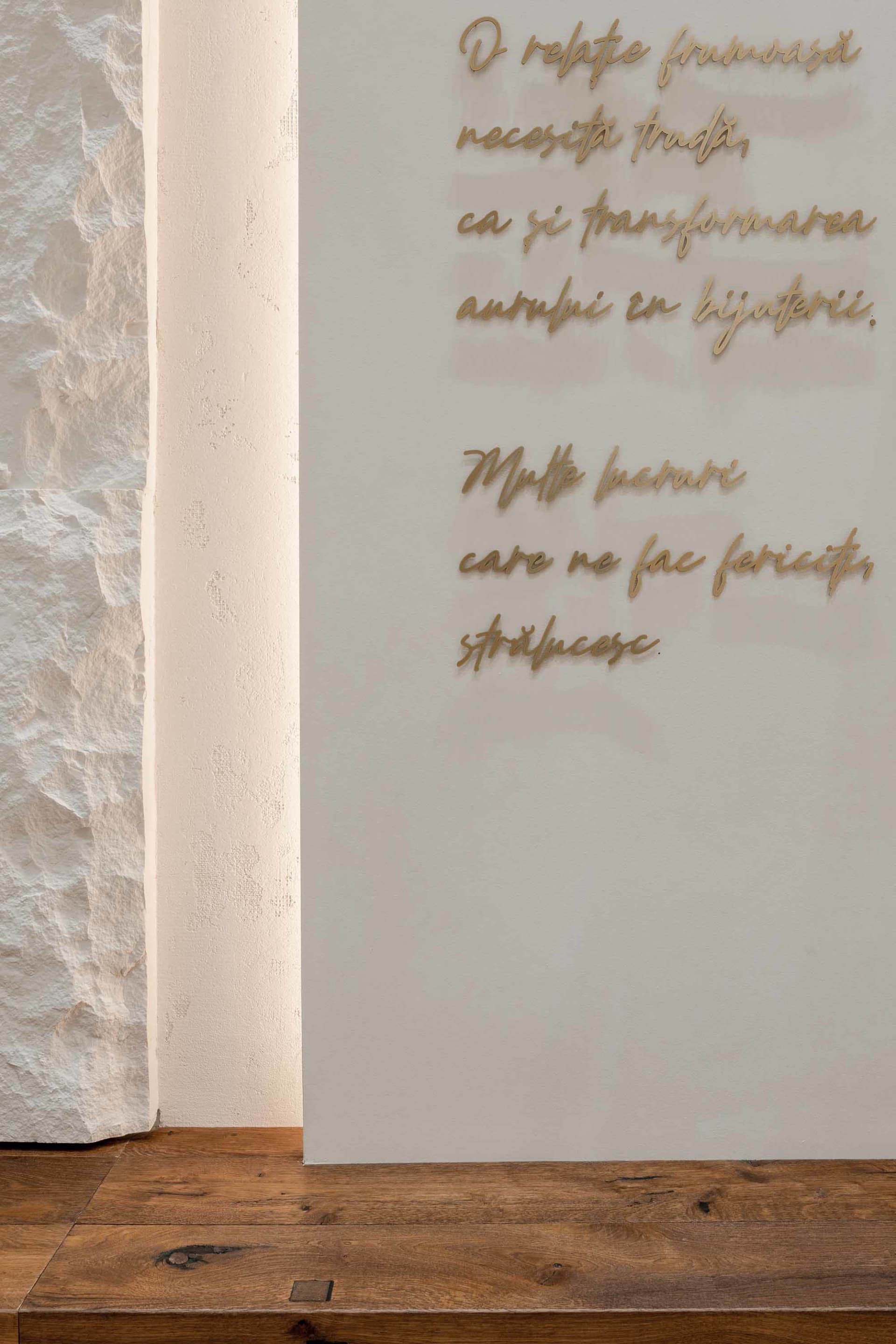 A wall with a quote displayed in cursive script, surrounded by a wooden floor and a textured stone wall.