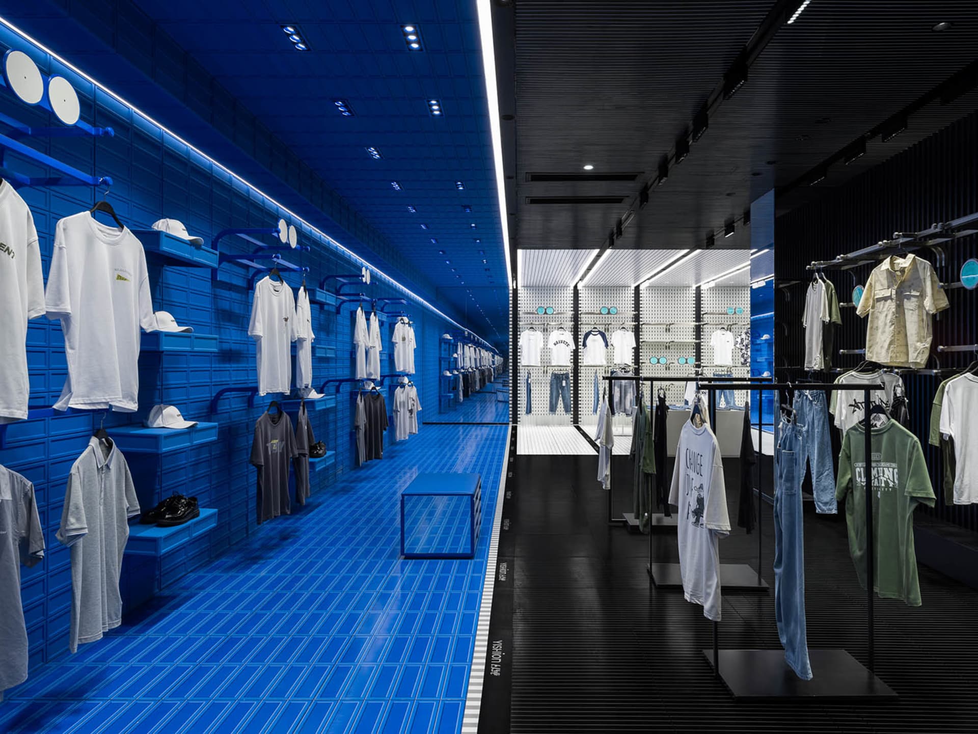 A retail interior with blue tiled walls and black metal fixtures showcasing clothing.