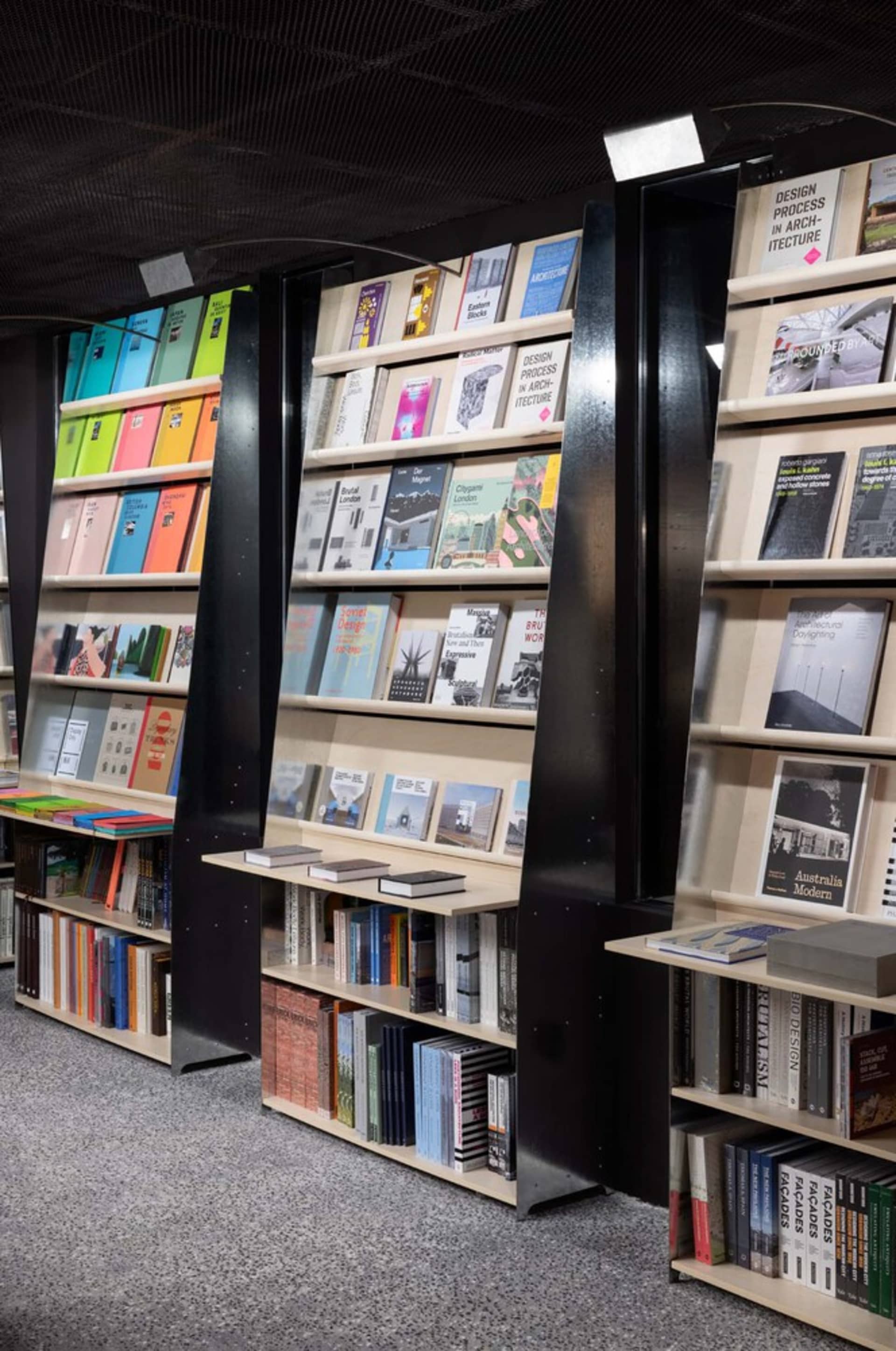 一間現代書店，擁有高聳流線的書架，陳列著色彩繽紛的書籍與建築類書籍。