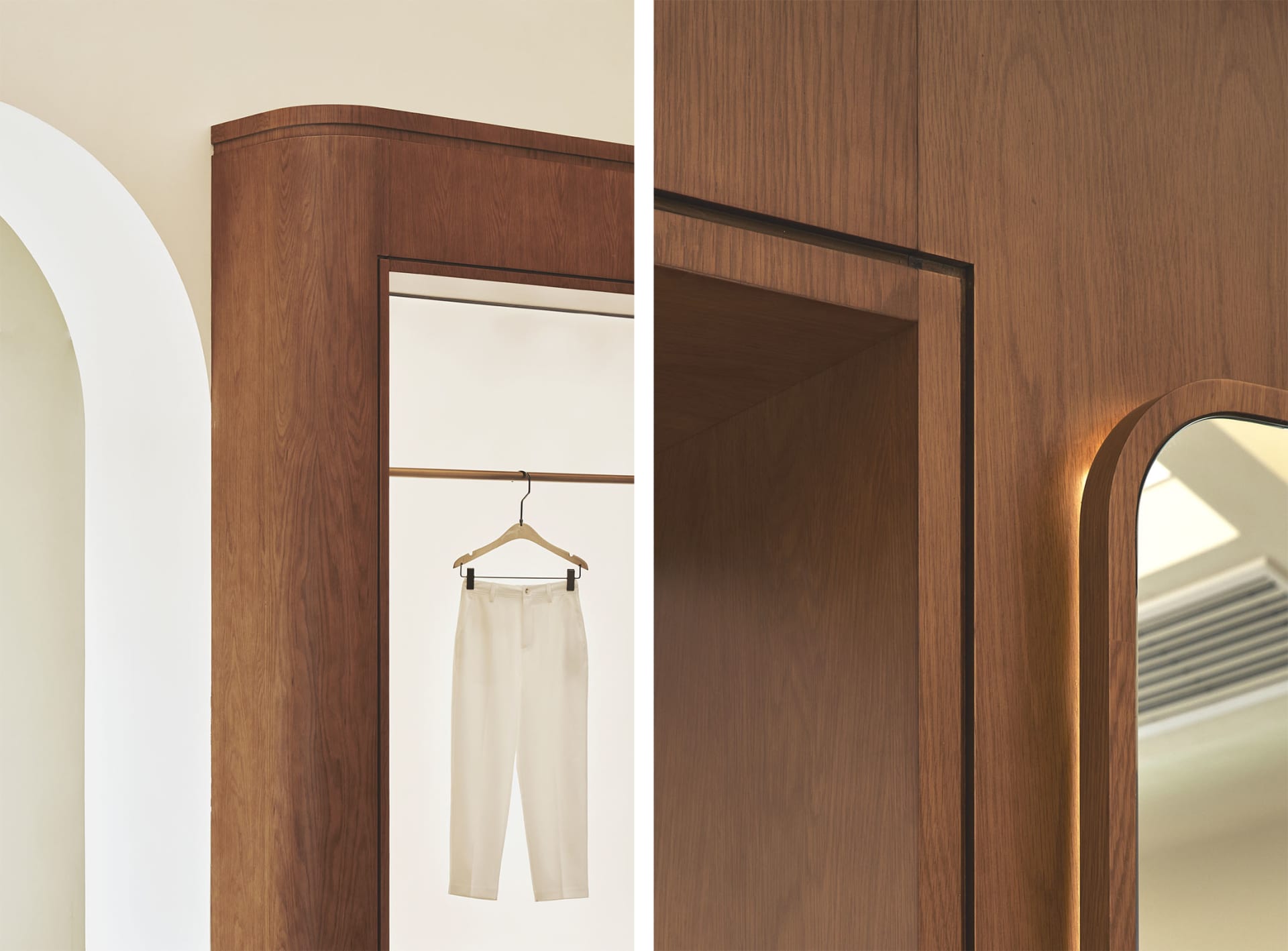 A minimalist clothing store interior with wooden panels, white trousers hanging on a metal rail, and an arched doorway.