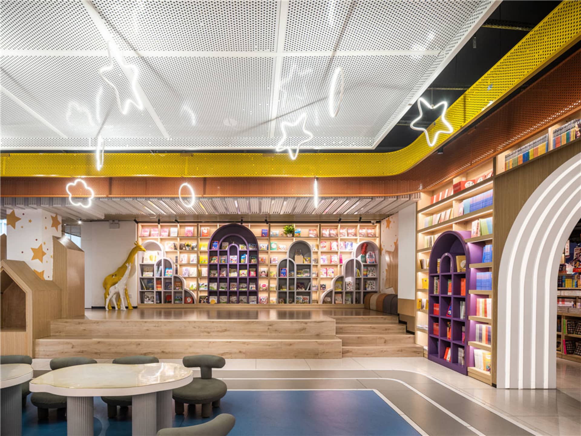 A modern children's library interior with colorful wooden shelves, bright neon signs, and a cozy seating area