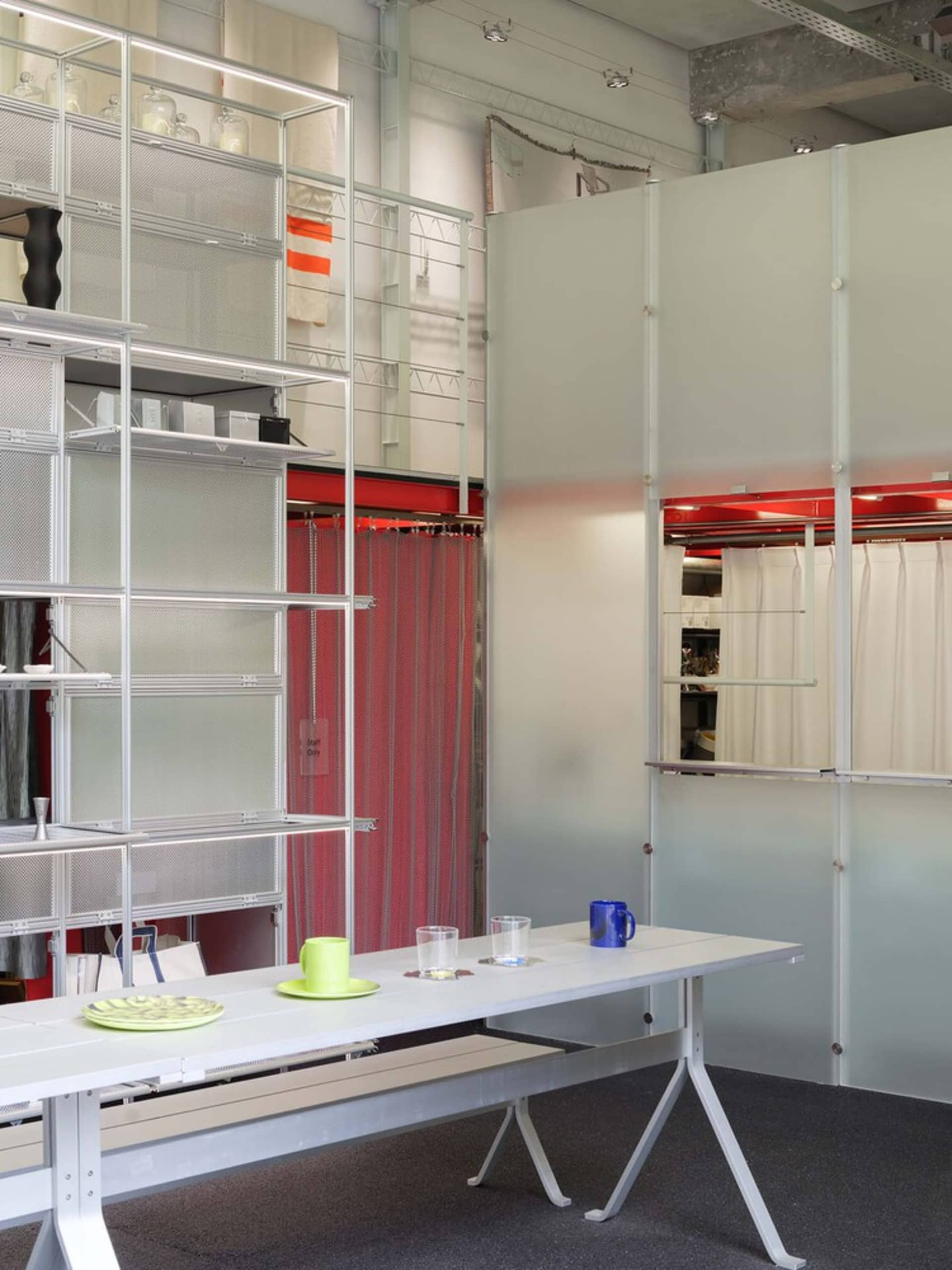 An industrial-style office space with metal shelving units and a long white desk with glassware.