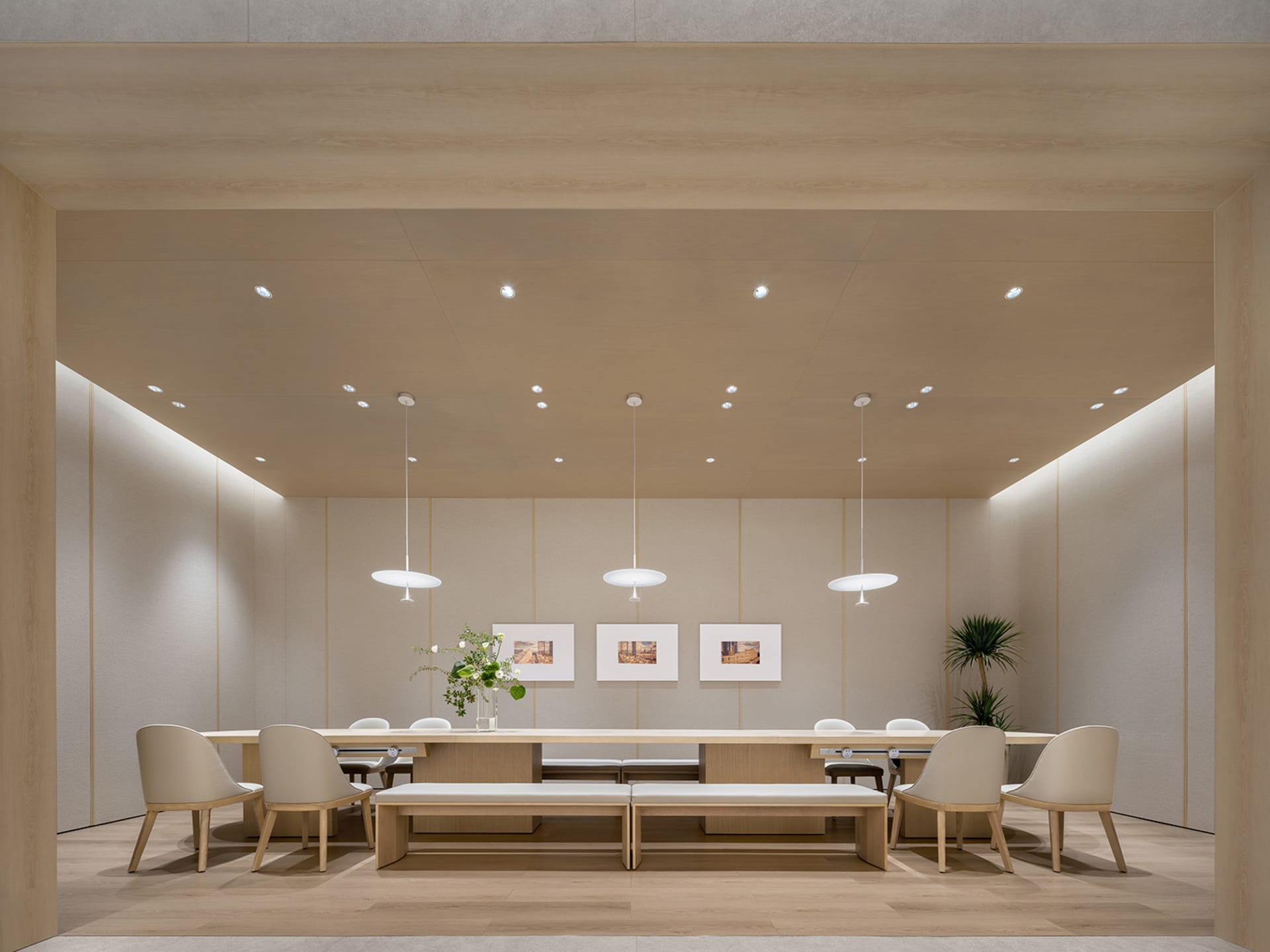 Modern meeting room with wooden tables, chairs, and benches, featuring minimalist design and natural lighting.
