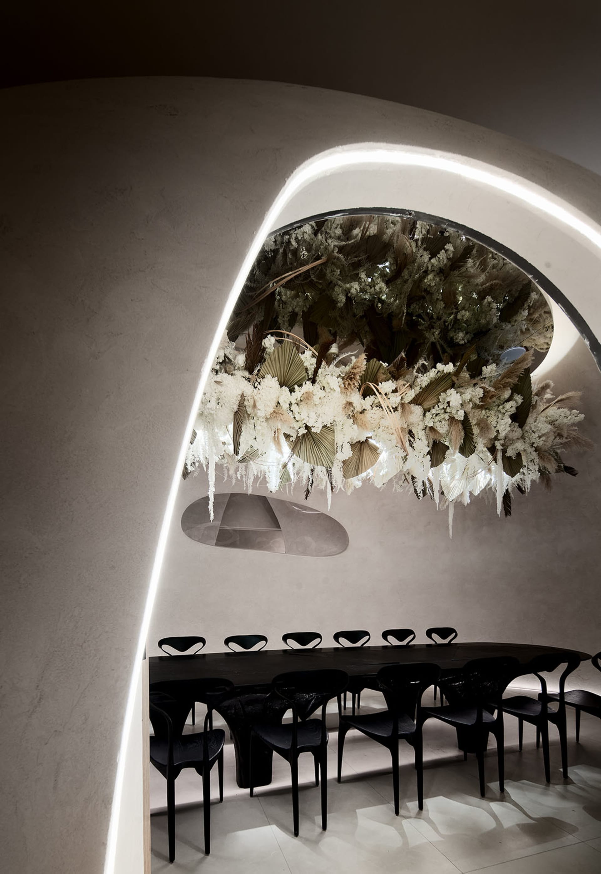 A minimalist restaurant interior featuring a large, intricate floral installation made of dried flowers and plants.