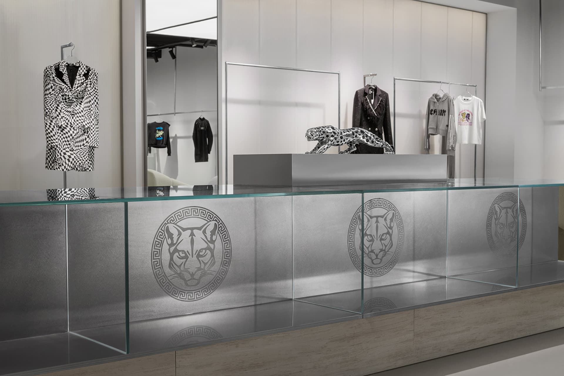 A retail clothing store display featuring a glass counter with a metal leopard statue and clothing items displayed on racks a