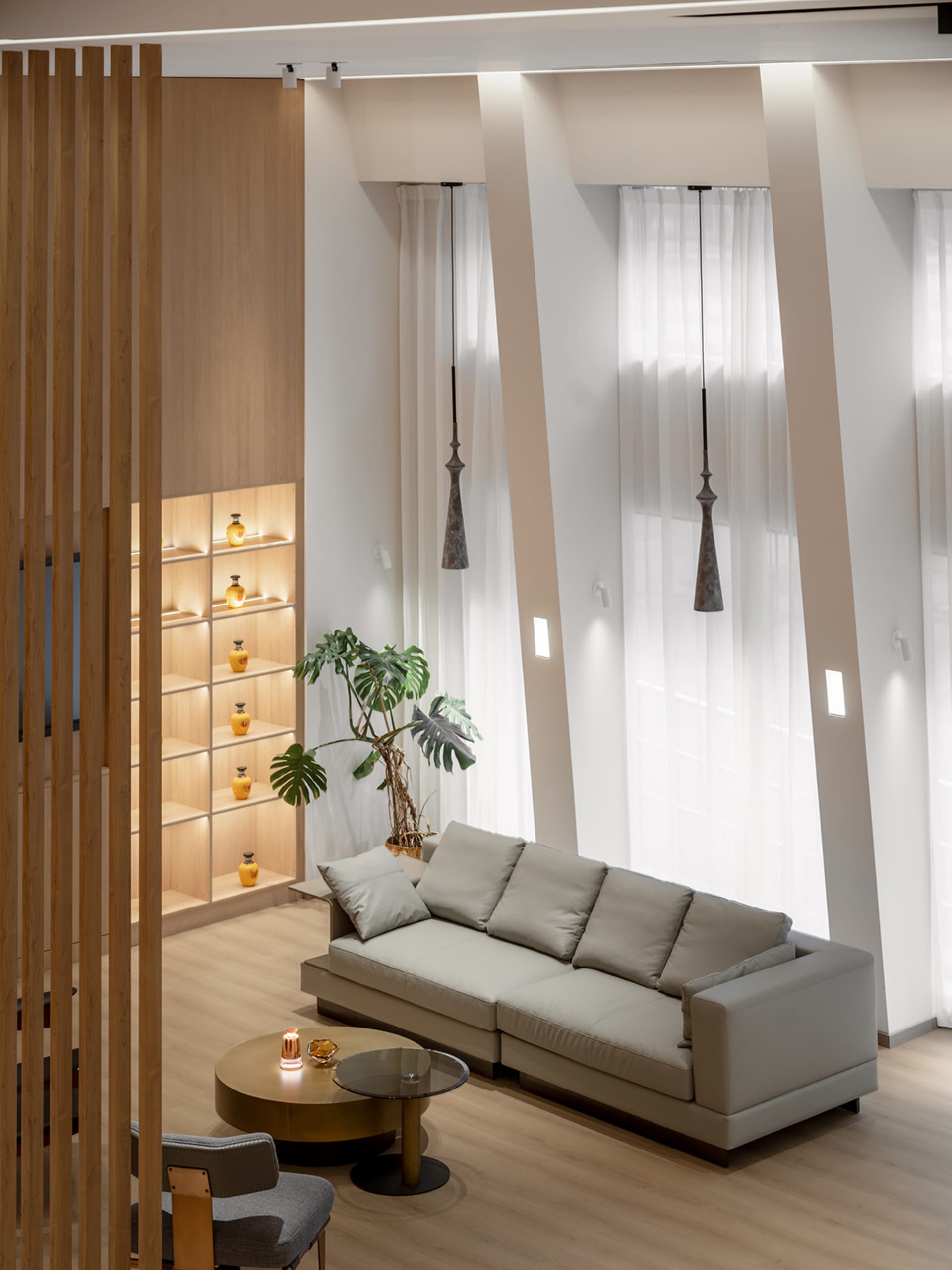 A minimalist living room with a beige sofa, glass coffee table, potted plant, and wooden bookshelf with ambient lighting.