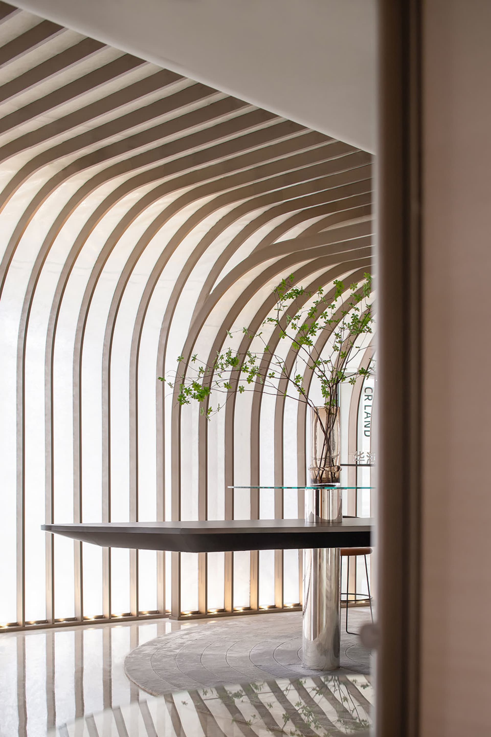 A modern interior space with glass walls and a polished floor, featuring a sleek table and decorative plant.