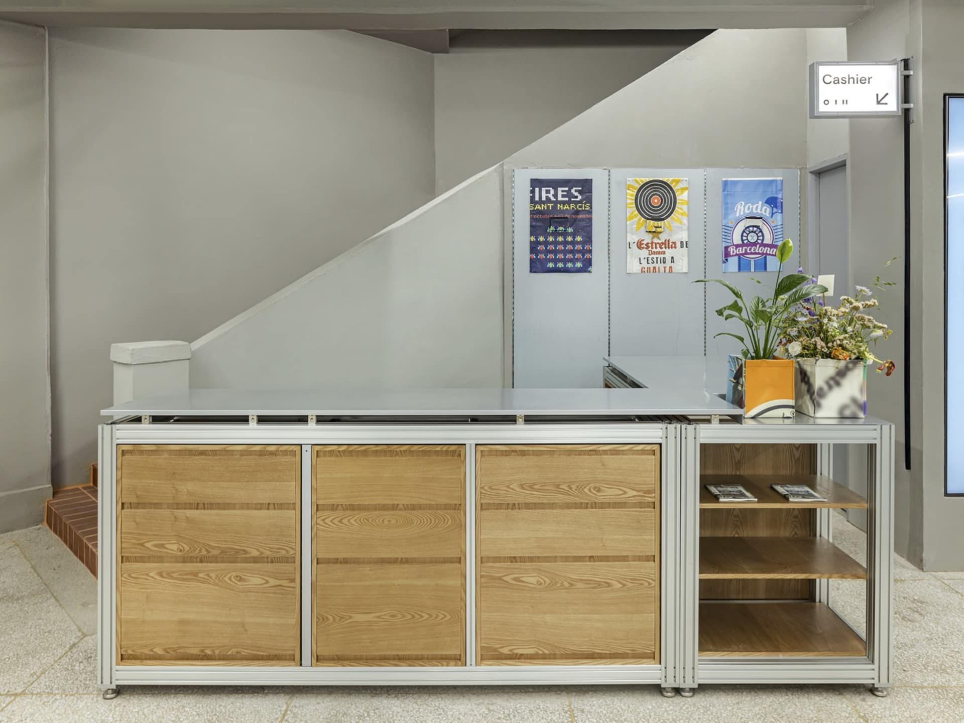 Modern reception desk with wooden drawers and metal frame, accompanied by potted plants.