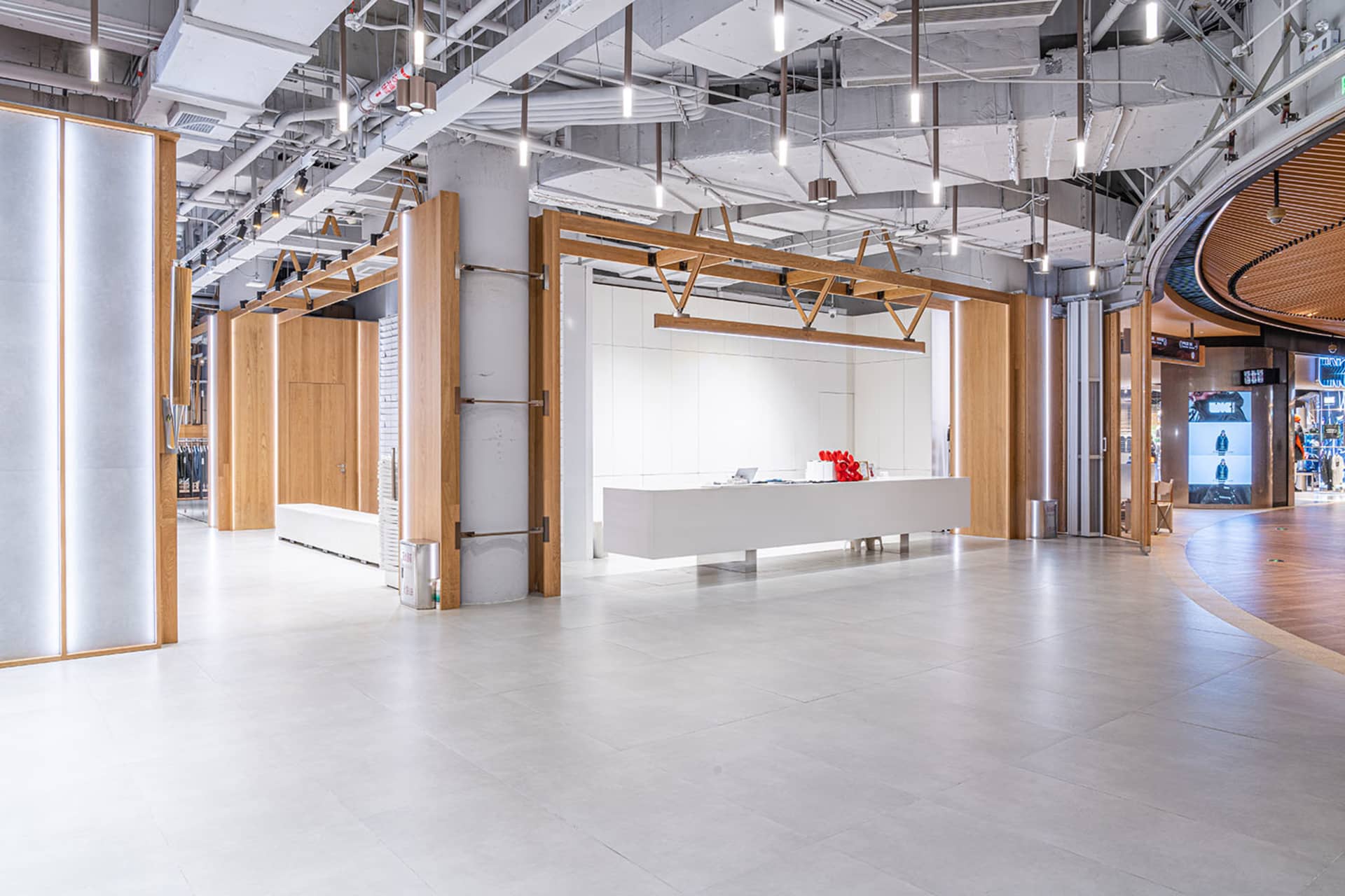 A modern interior of a shopping mall with clean lines, white floors, and wooden accents.