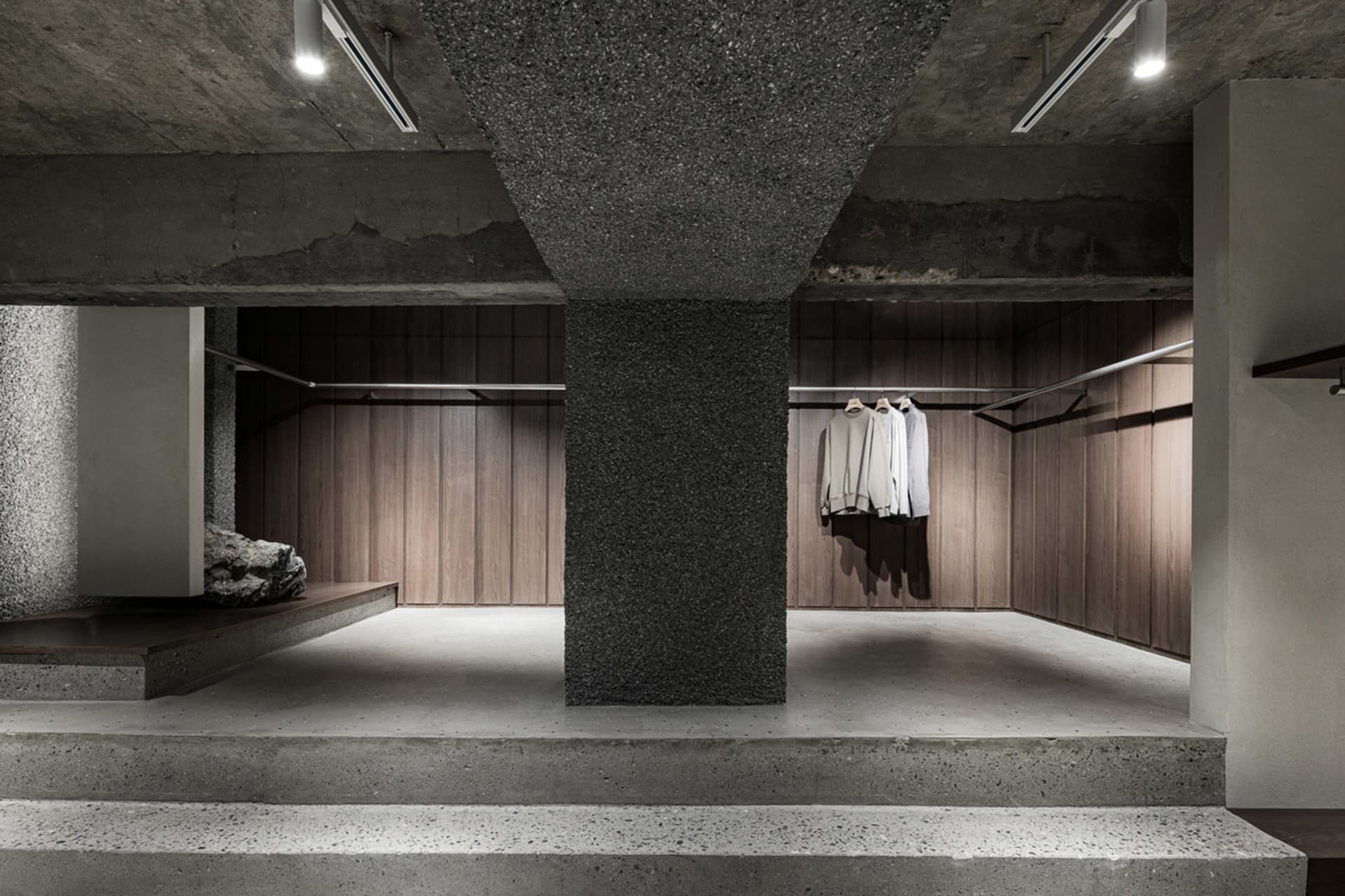 A minimalist clothing boutique with concrete flooring and wooden clothing racks.