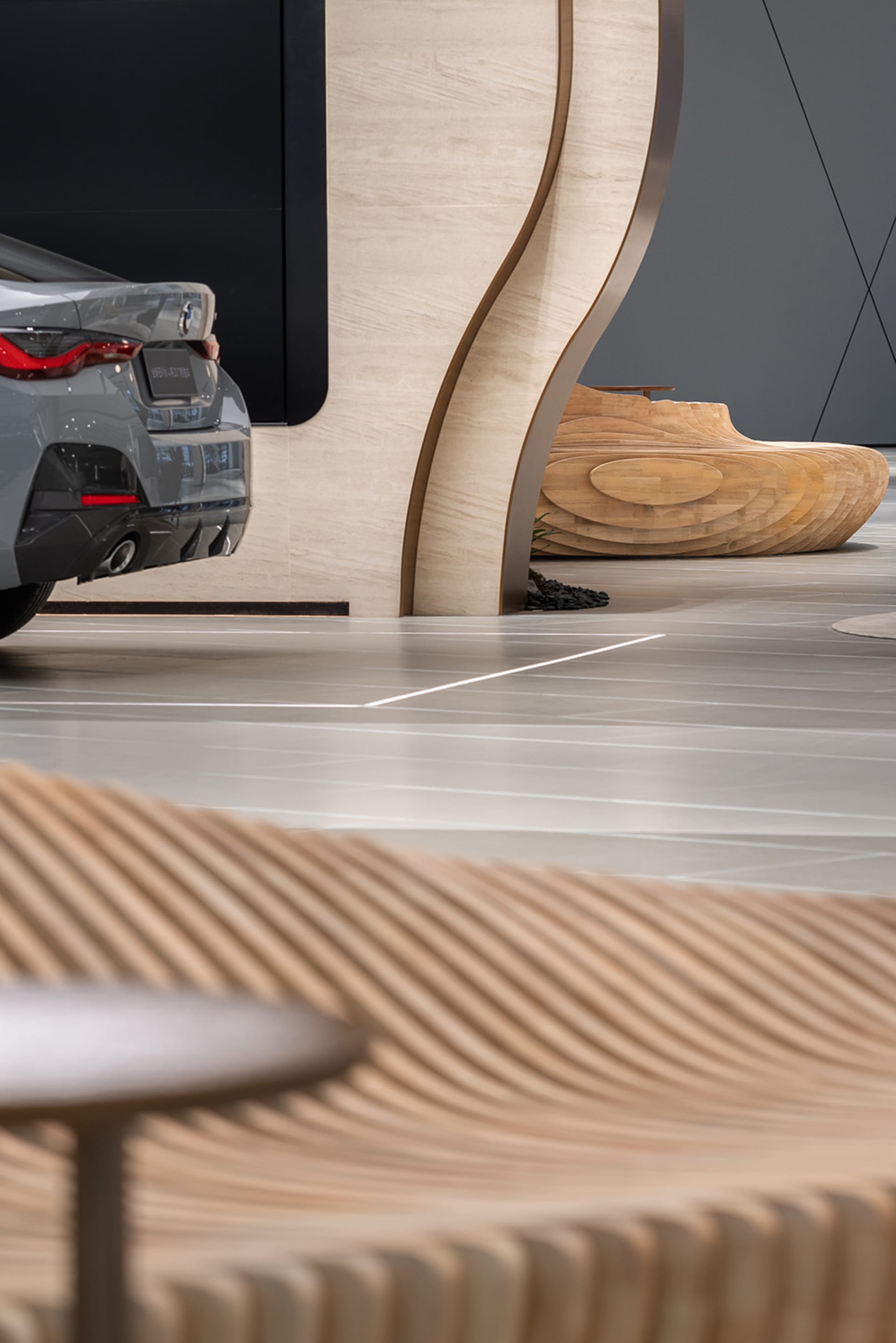 Modern showroom with concrete elements showcasing a sleek car and contemporary seating.