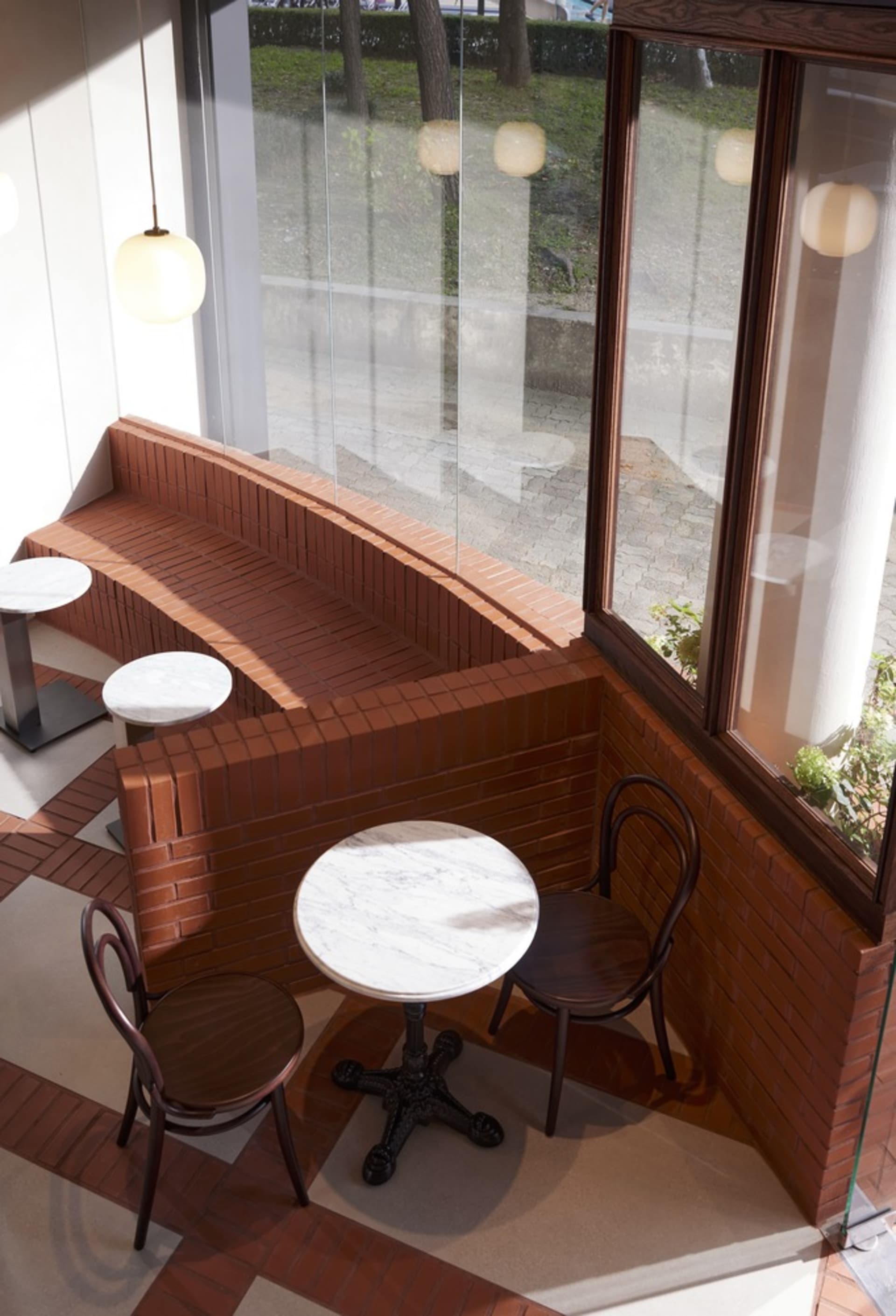 Circular marble table with vintage wood chairs, set in a cozy cafe window seat with brick walls and a view outside through la