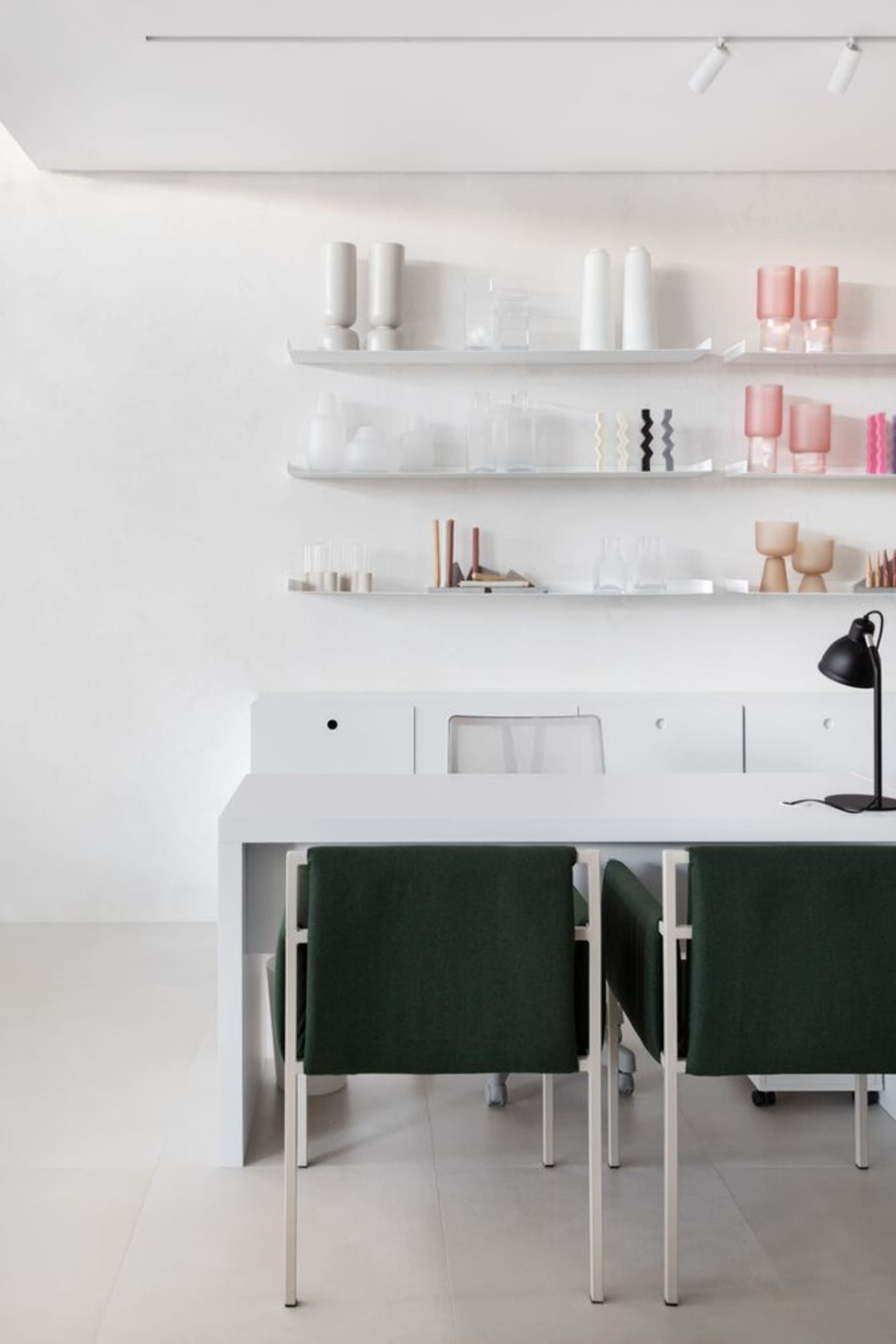 A minimalist home office featuring white shelves and chairs with green upholstery.