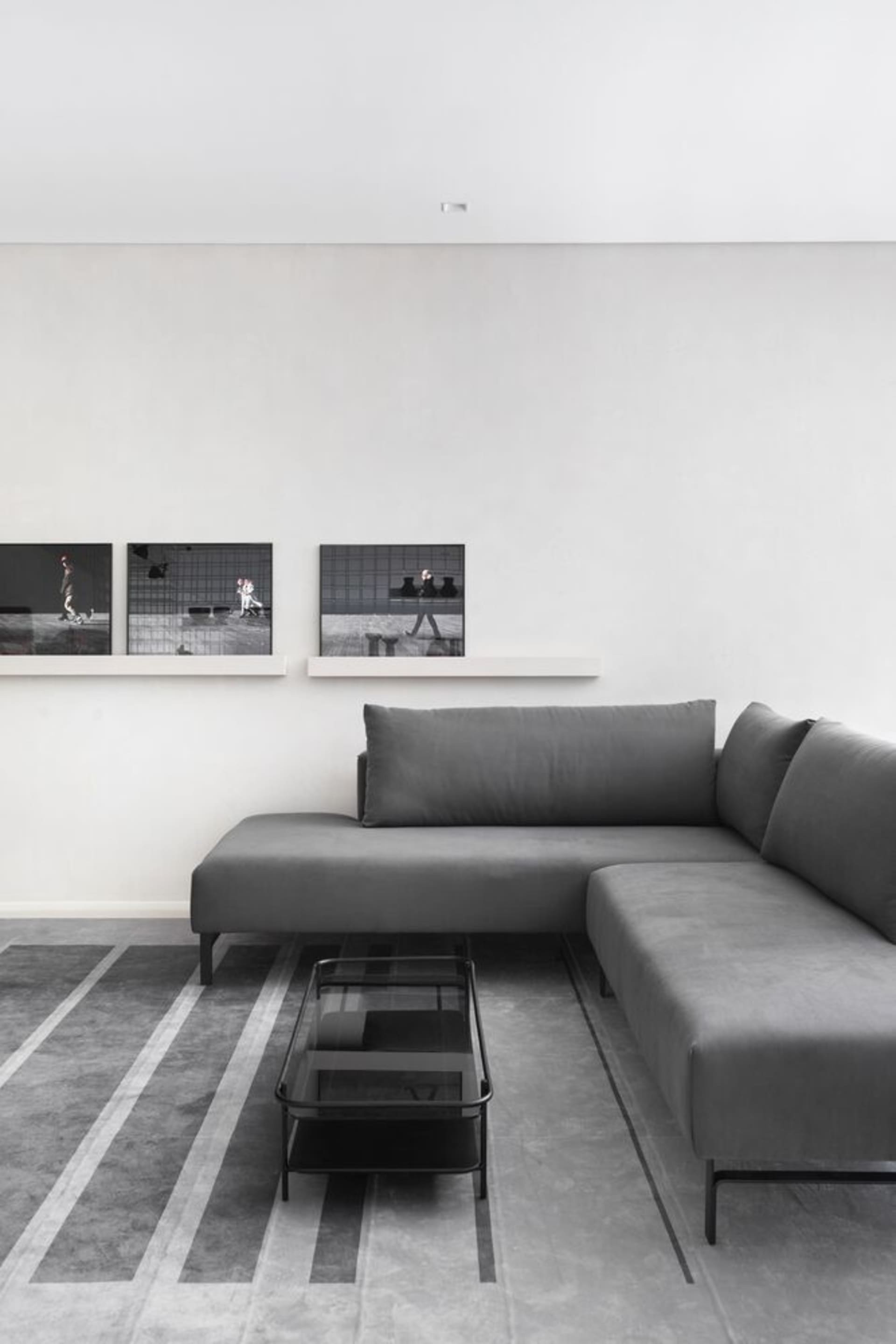 A minimalist living room featuring a gray sectional sofa on a patterned concrete floor, with a glass coffee table and framed