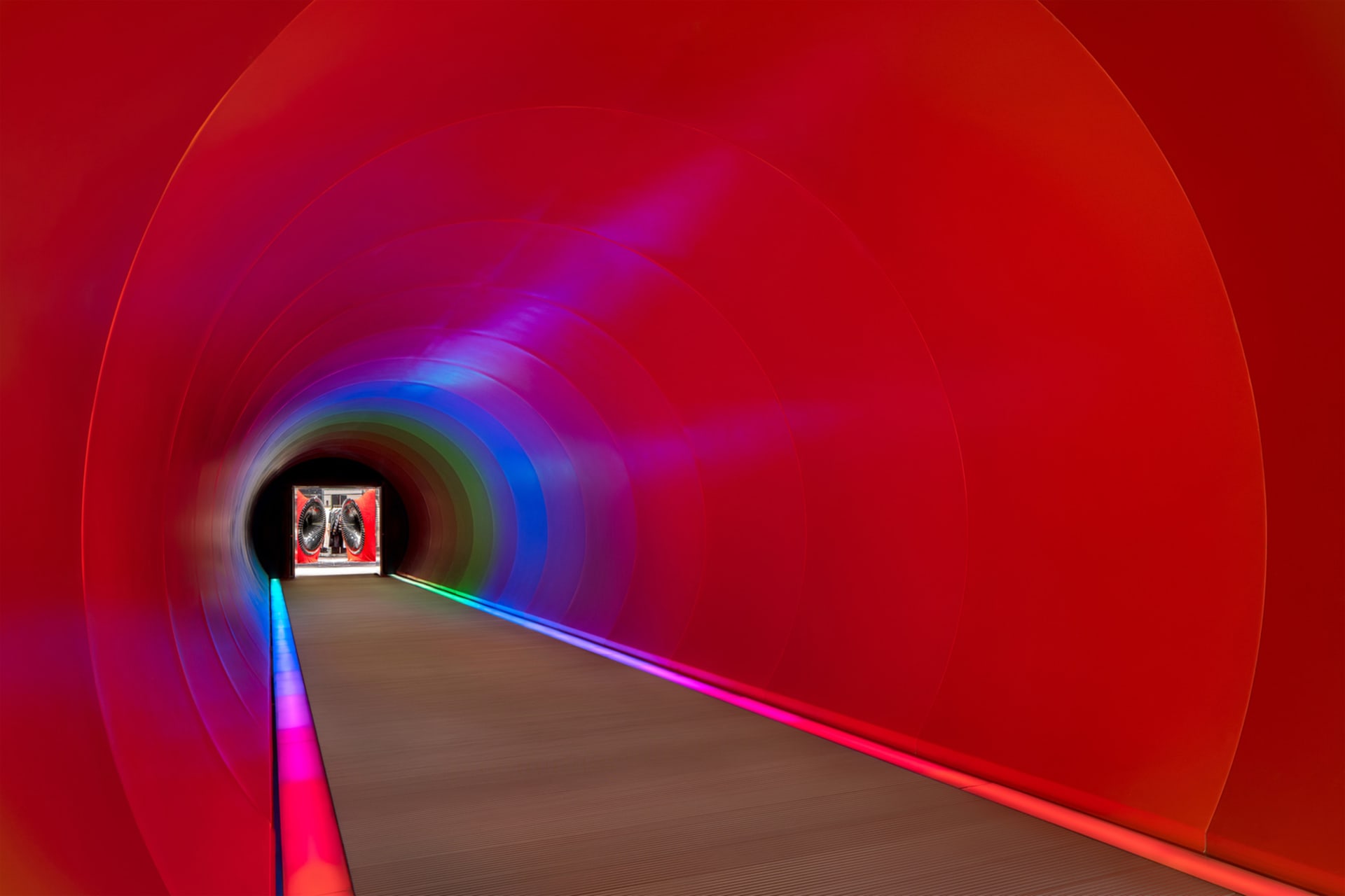 A modern, red metal tunnel illuminated with colorful lights.