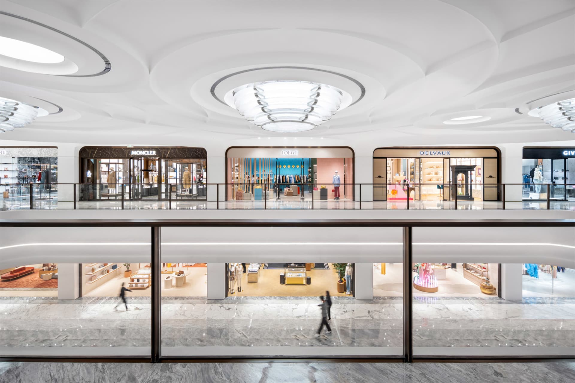 Shopping mall interior with white marble floors and walls, featuring luxury retail storefronts with glass fronts against roun