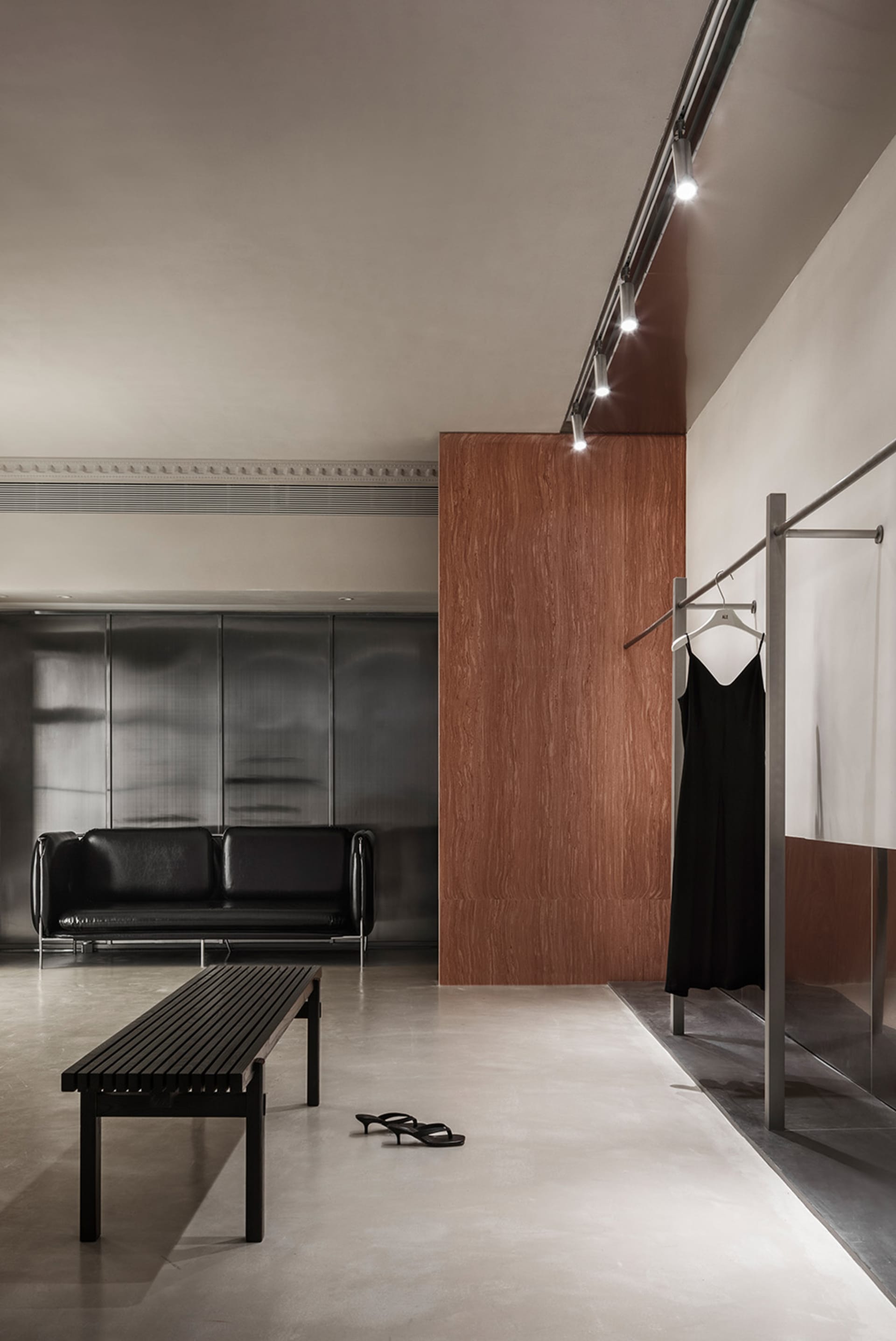 A modern fashion store interior featuring concrete flooring, a minimalist black sofa, a black wooden bench, and a hanging bla