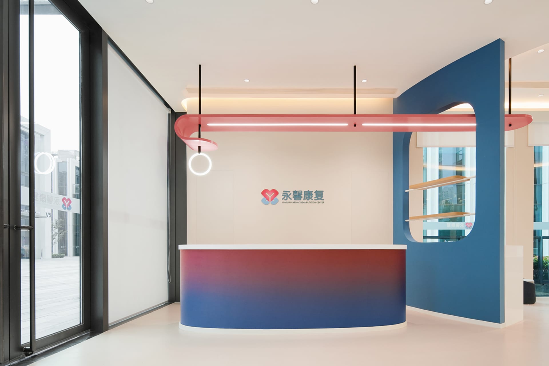 一座現代接待櫃台，搭配紅藍漸層、吊燈燈具，以及品牌標誌。