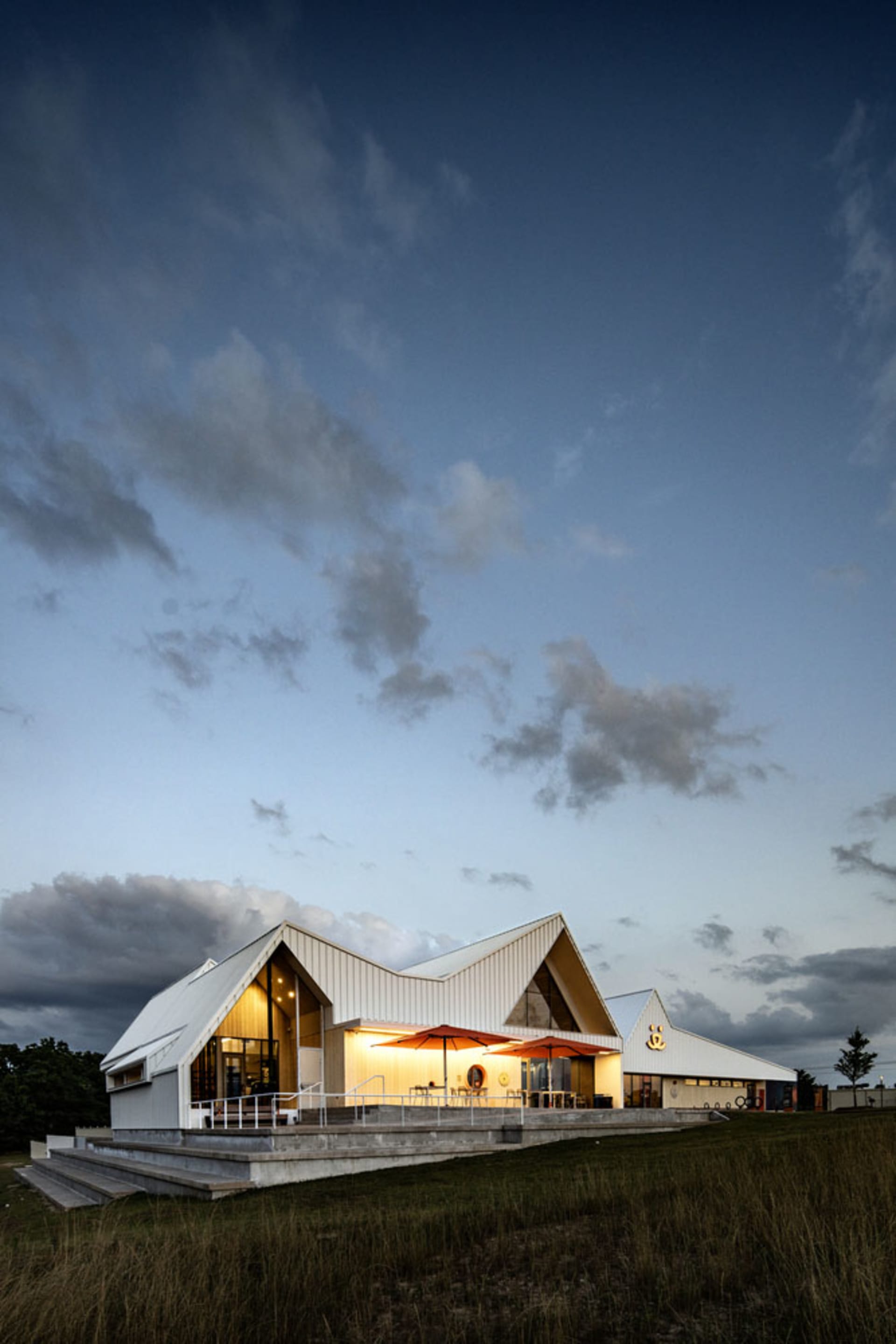 Modern commercial building with metal-clad angled roof, illuminated exterior at dusk with cloudy sky