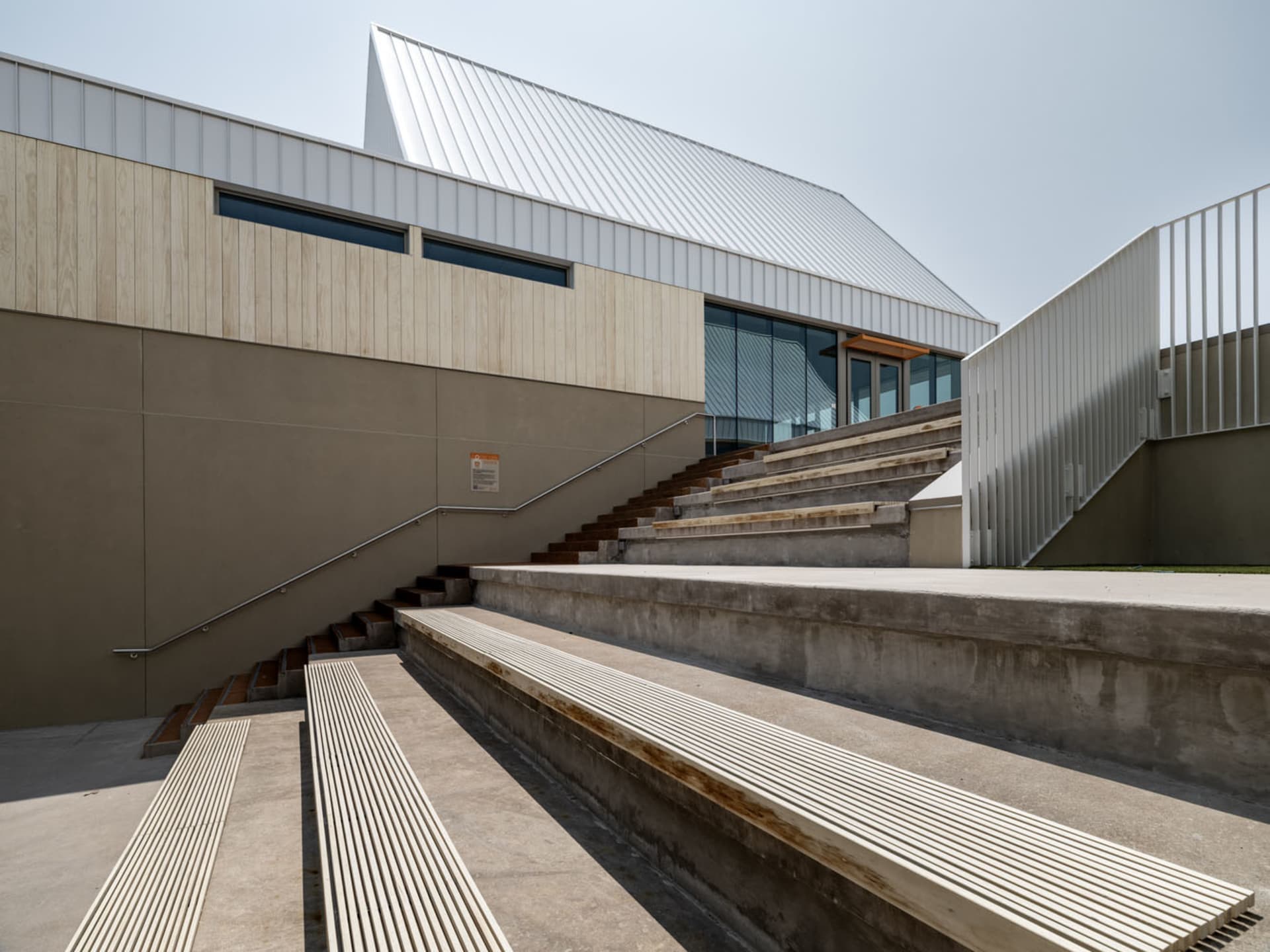 A modern architectural structure with metal roof, wooden elements, and concrete seating areas.