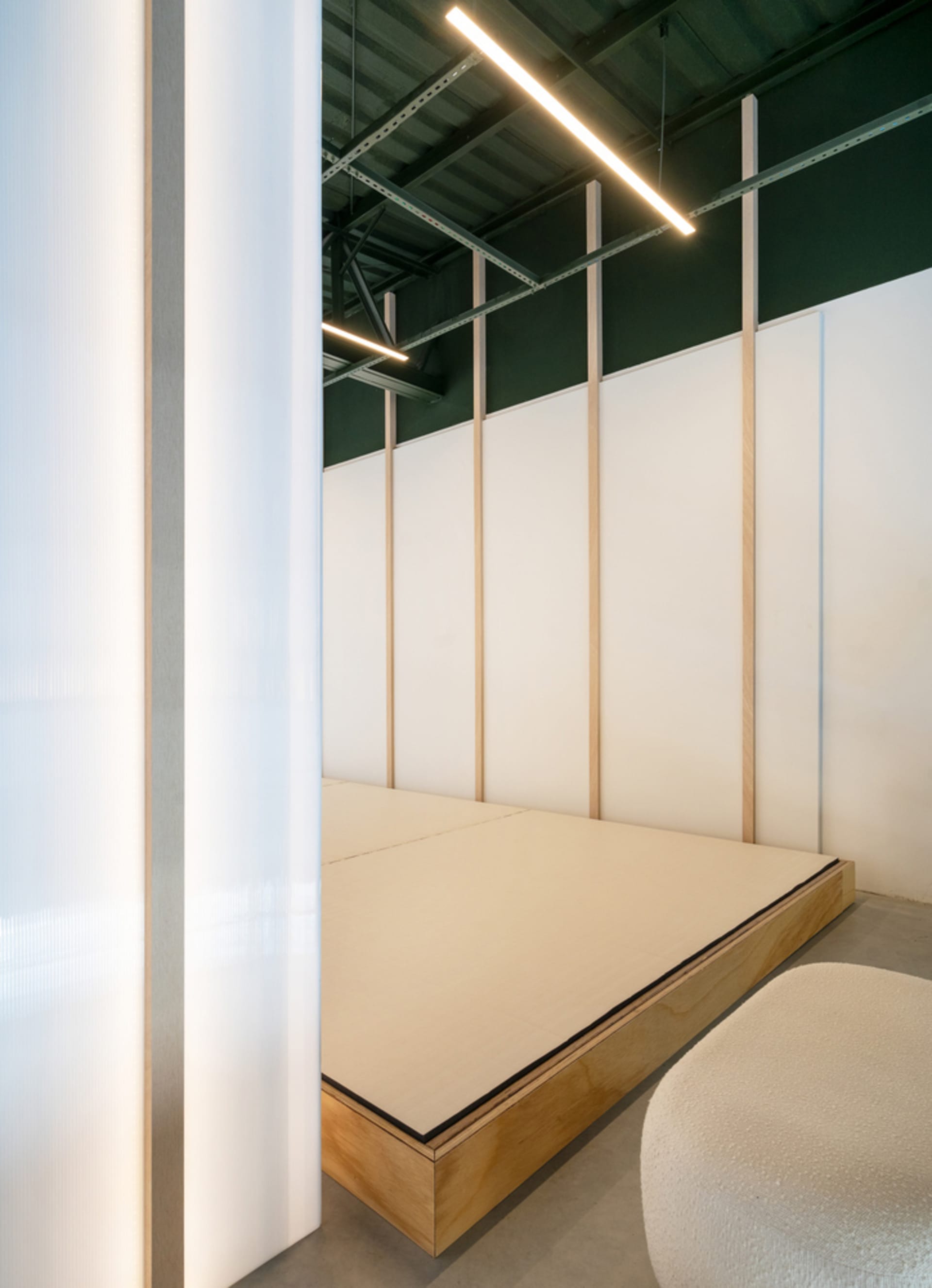 A minimalist bedroom featuring white textured walls and a beige wooden platform bed.