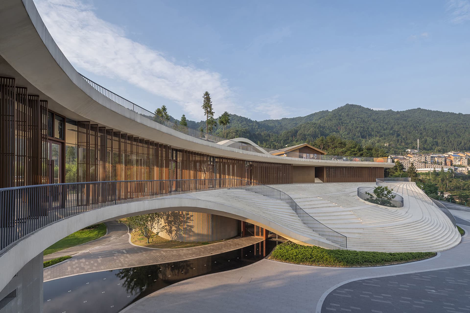 A modern pavilion constructed from concrete with a curved roof and surrounding greenery.