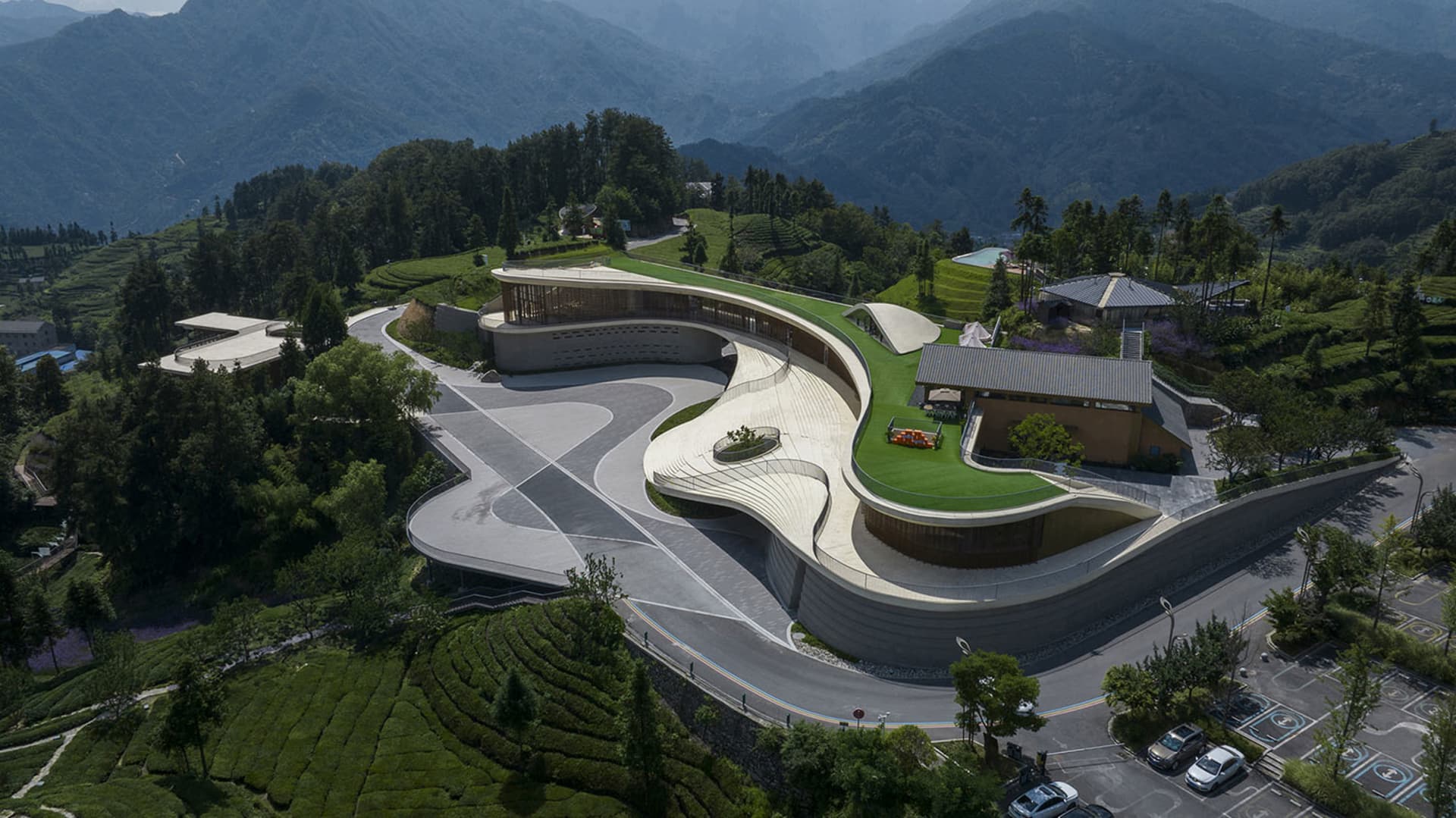 A modern building with a concrete exterior surrounded by lush greenery and mountains.