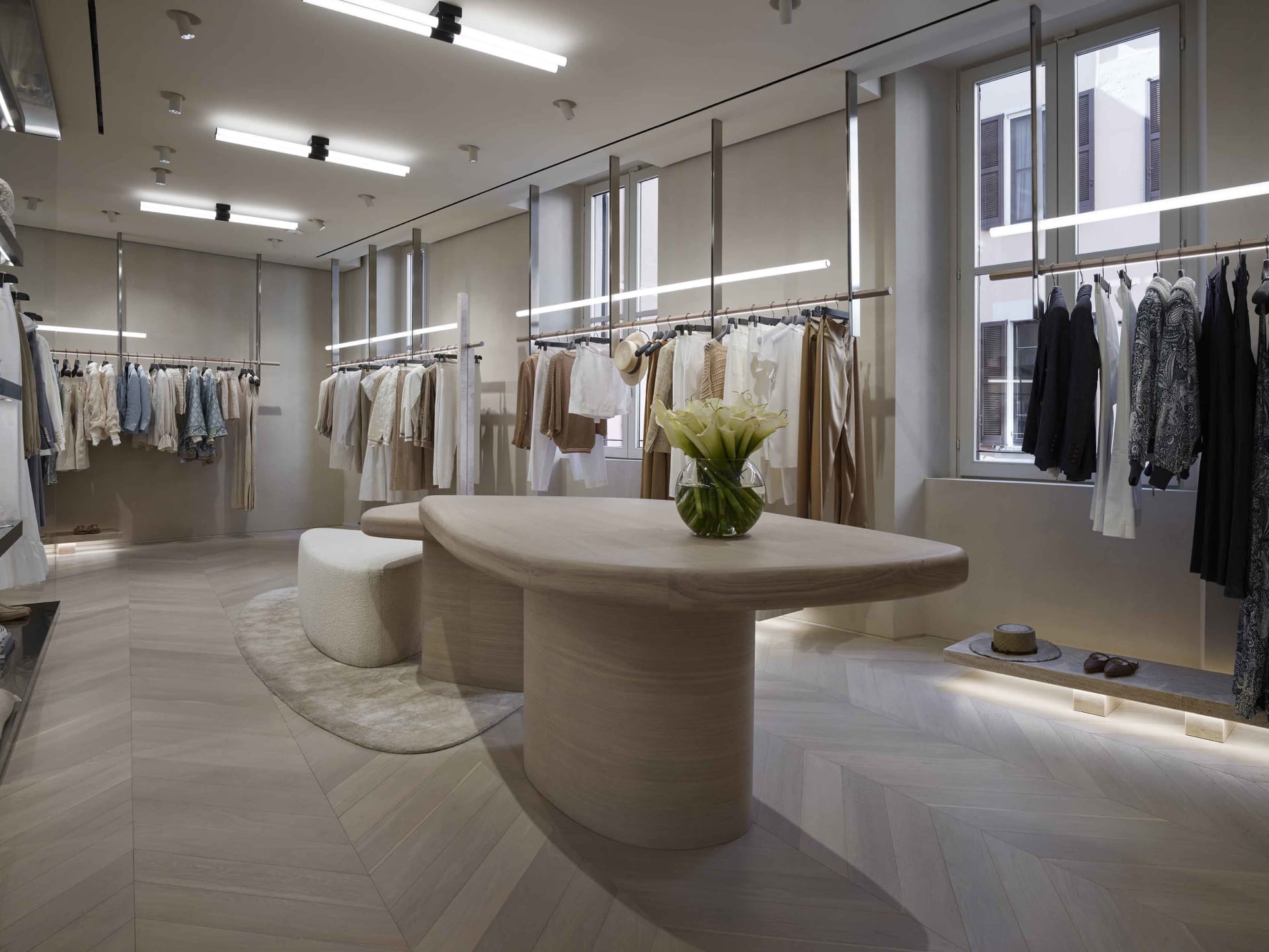Modern retail store with clothing racks, a wooden central table, and a glass vase with flowers.