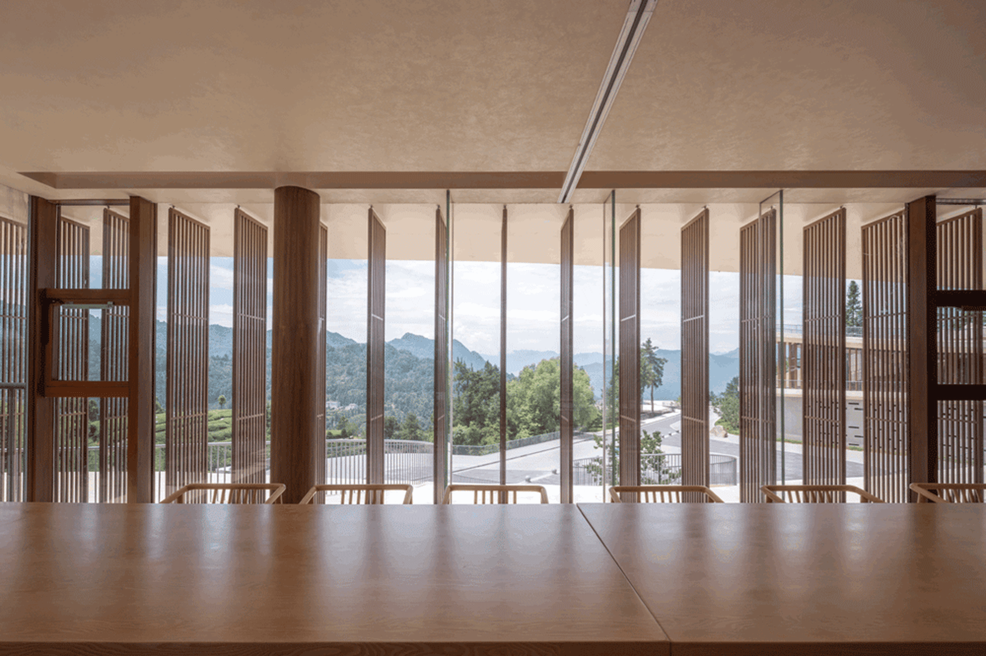 Modern restaurant interior with wooden counter and seating area overlooking scenic mountains.
