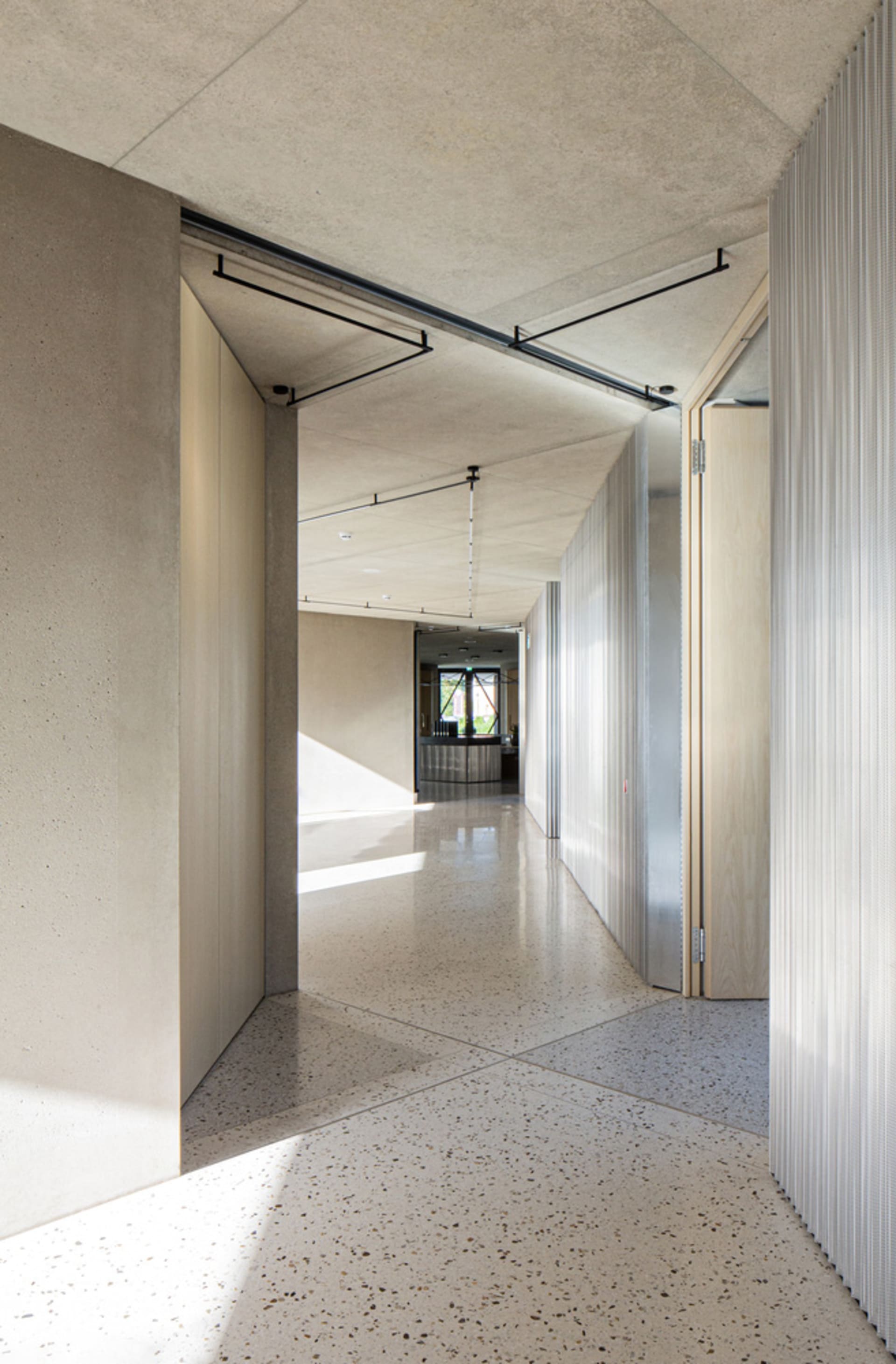 Modern minimalist office interior featuring concrete walls and floors, with natural light entering through large windows.