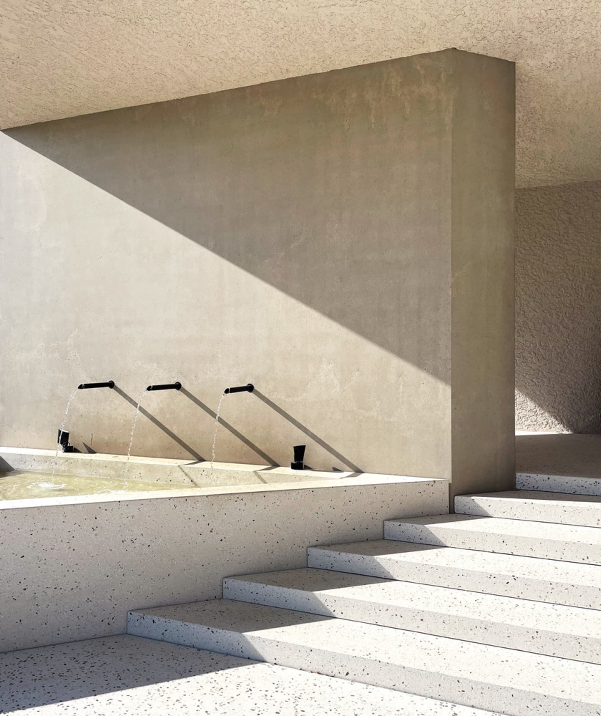 A minimalist outdoor water fountain with concrete and terrazzo materials.