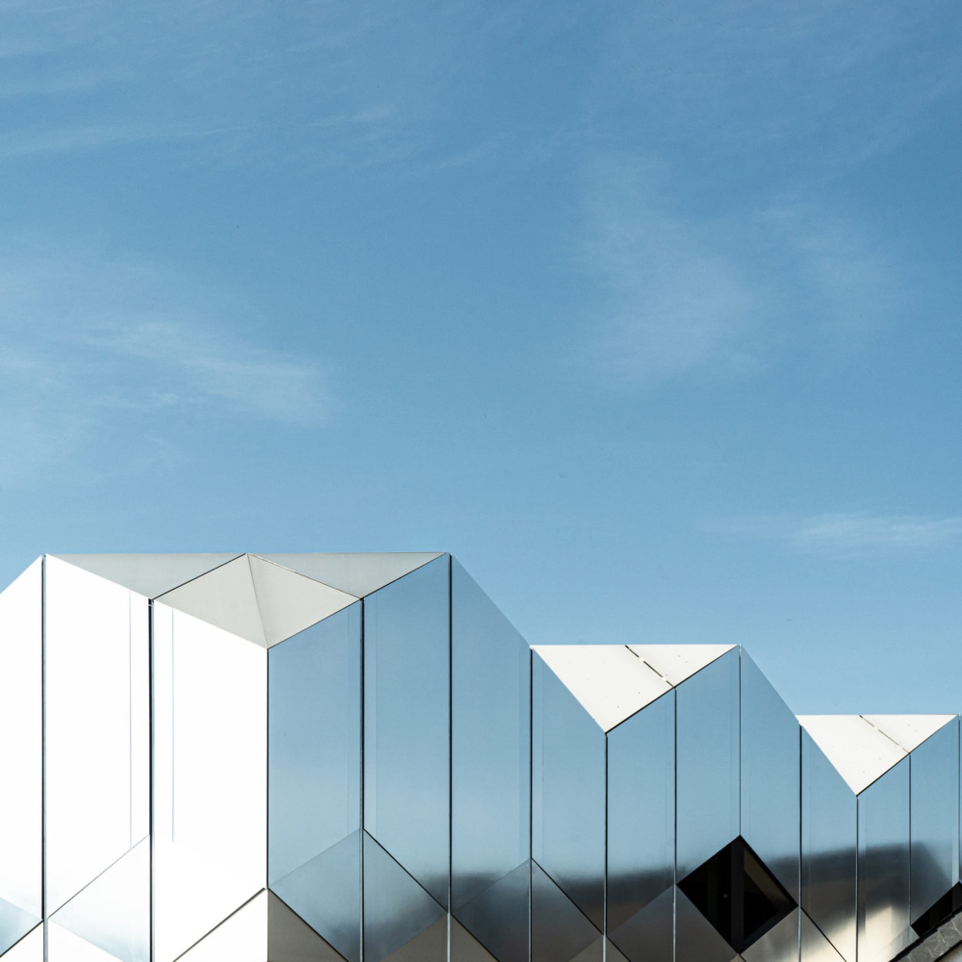 Modern building facade covered in reflective, mirrored glass panels against a clear blue sky.