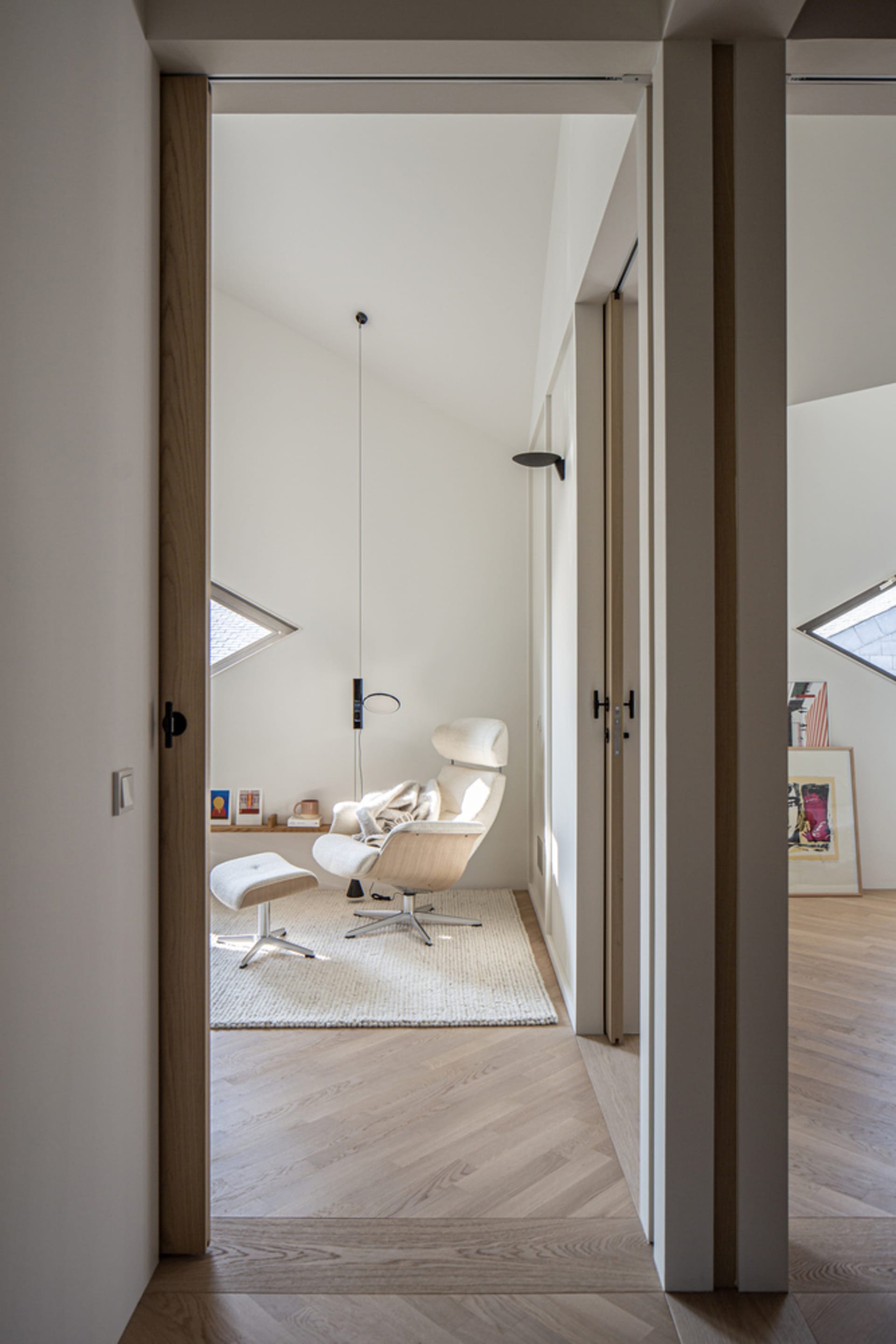 A modern minimalist living room with a wood floor, white walls, and a single white chair with a matching ottoman.
