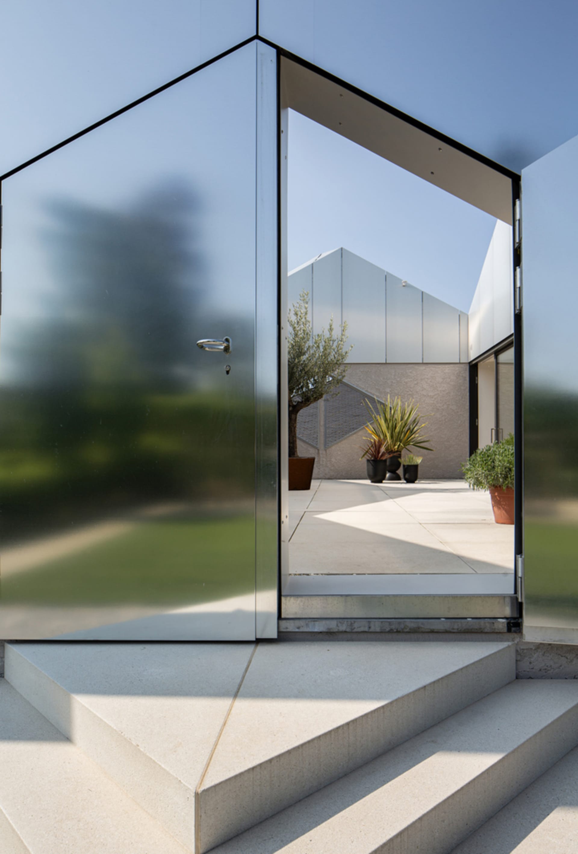 A modern glass exterior with a patio and potted plants.