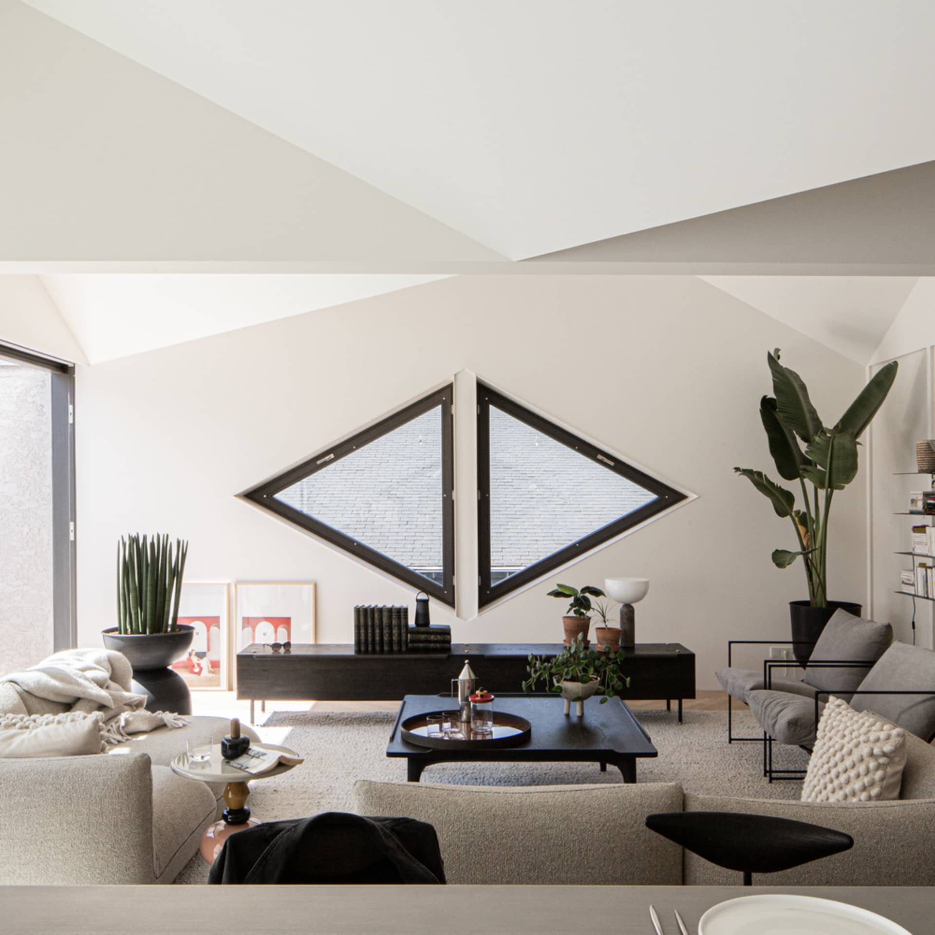 A modern minimalist living room with white and black decor, featuring a large diamond-shaped window and a wooden coffee table