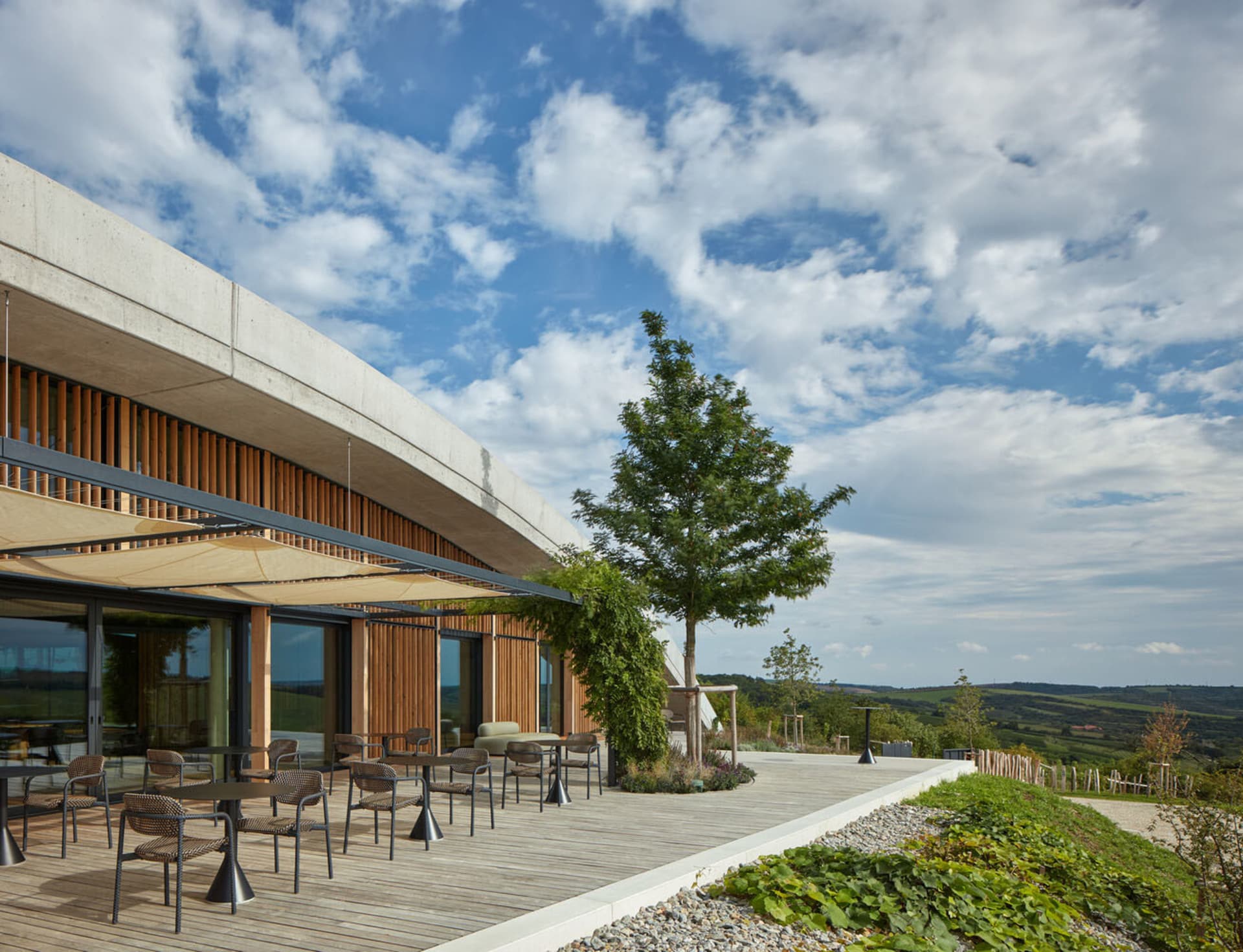 Outdoor seating area with tables and chairs on a wooden deck overlooking scenic hills.