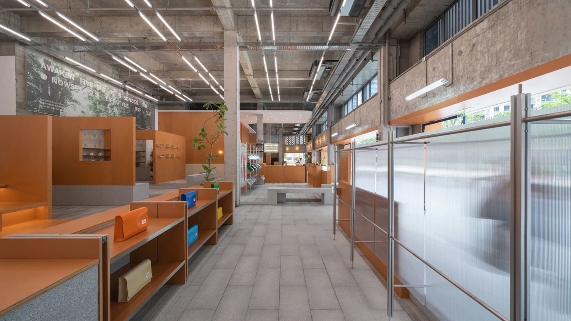A modern retail storefront with orange metal structures, concrete floors, potted plants, and a minimalist design.