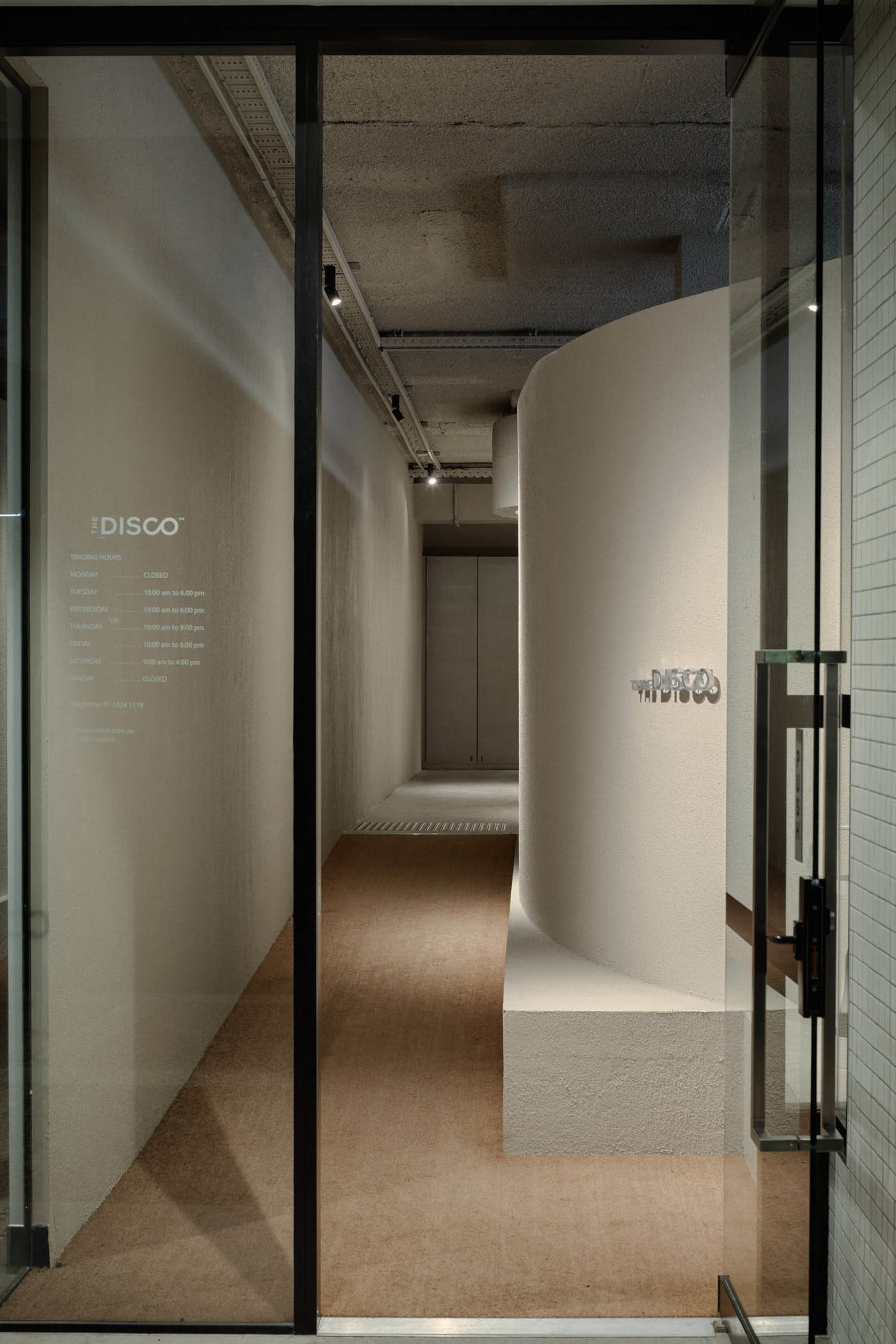 A modern office hallway with a concrete pathway lined by gray-colored walls and a reception desk.