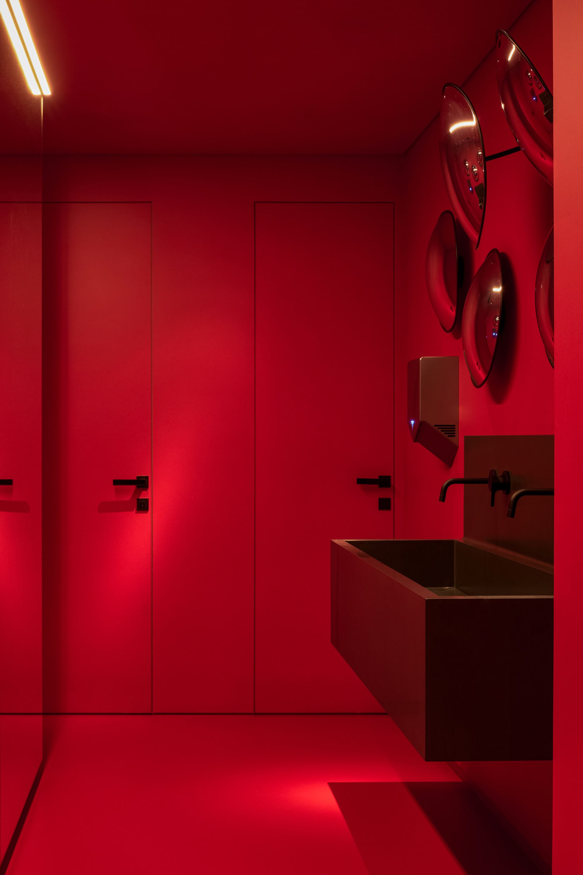 Modern minimalist bathroom with red walls and floor, black fixtures, and black light strip on the ceiling.