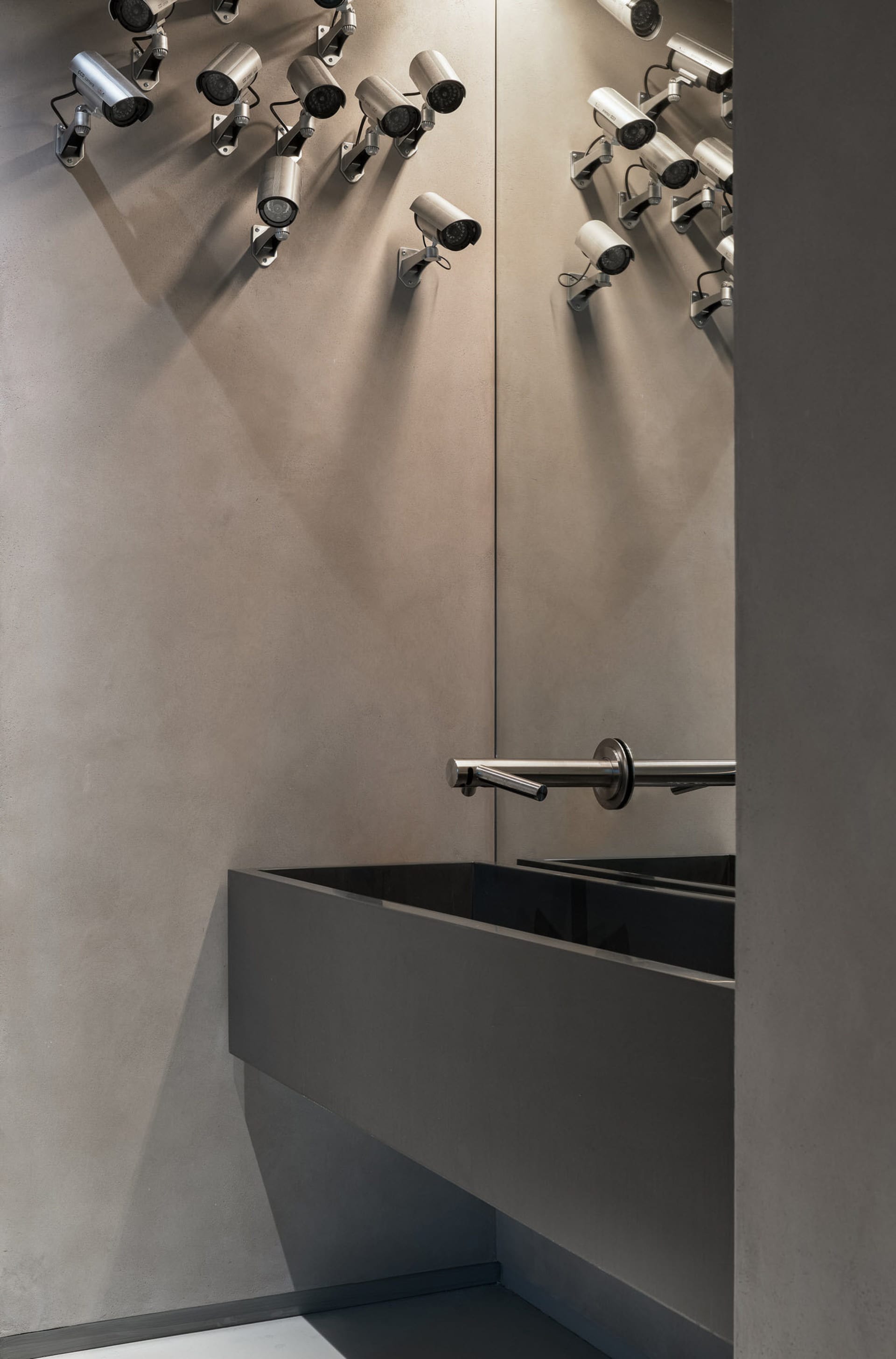 A modern bathroom with concrete walls, a sink, and numerous surveillance cameras on the walls.