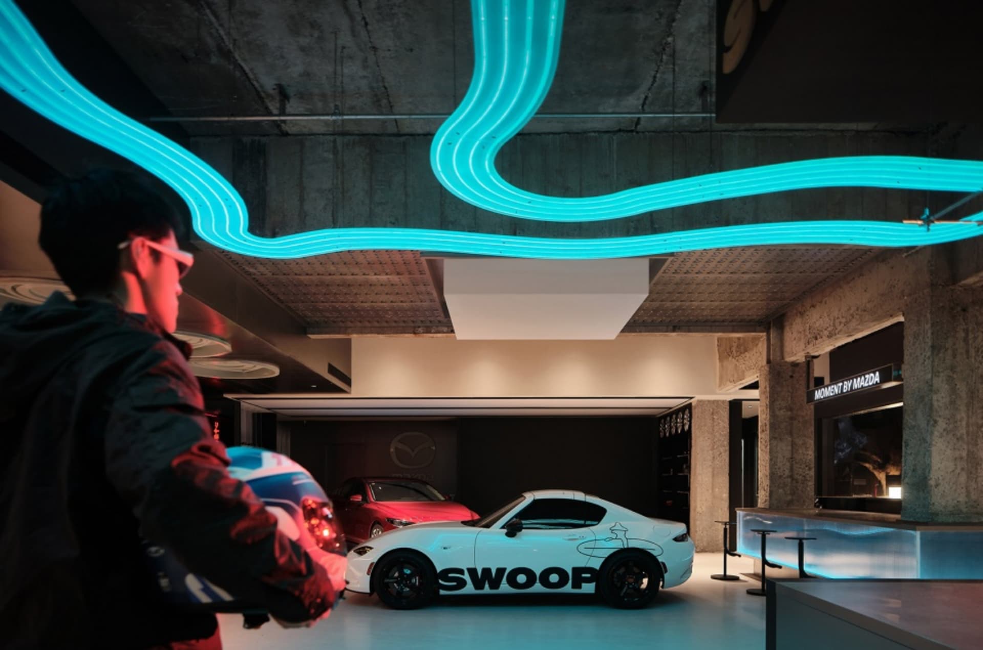 A modern showroom with a white car featuring 'SWOOP' and bright neon lights.