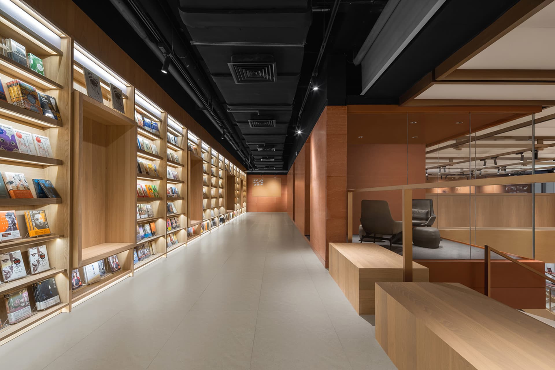 A modern library with wooden shelves, illuminated by LED lights, featuring a mix of books and magazines, and a seating area w